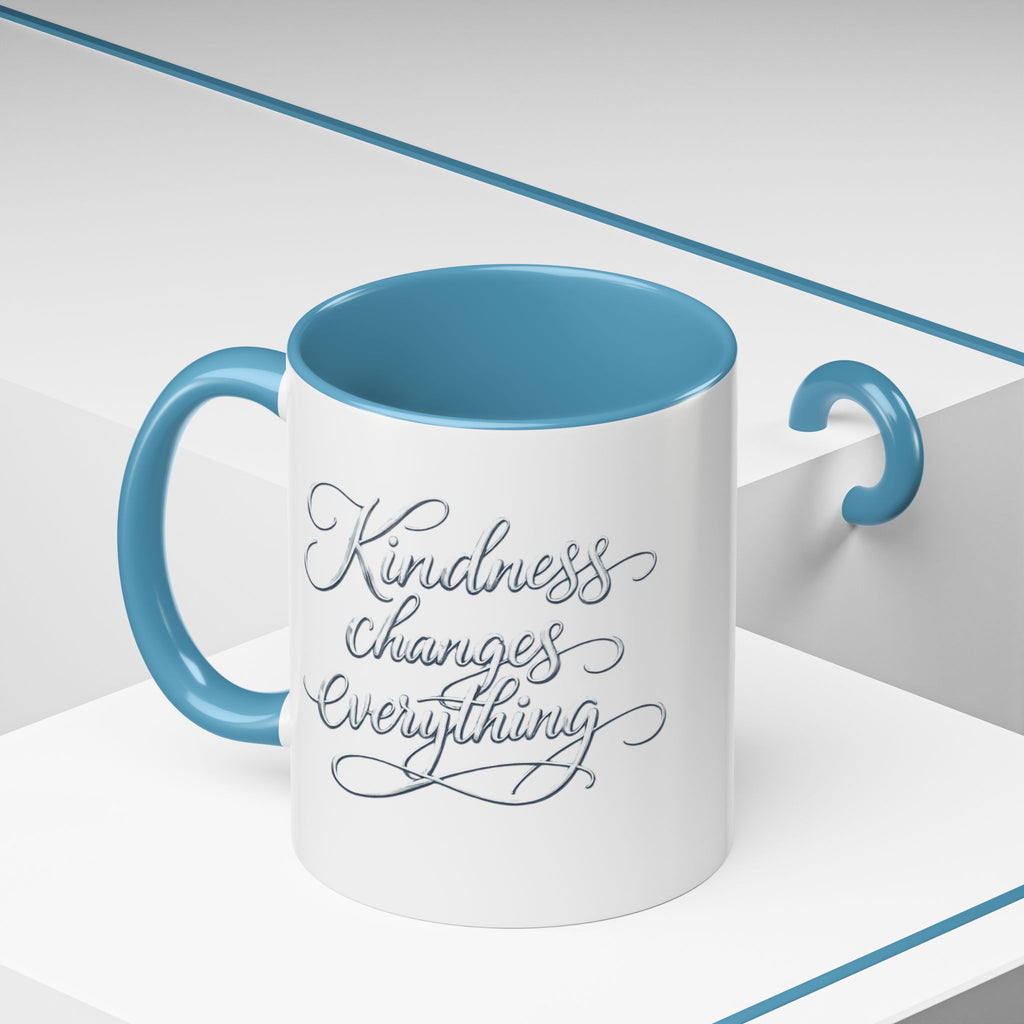 Inspirational ceramic accent coffee mug featuring elegant silver hand-lettered “Kindness Changes Everything” typography with colorful handle and interior accents.