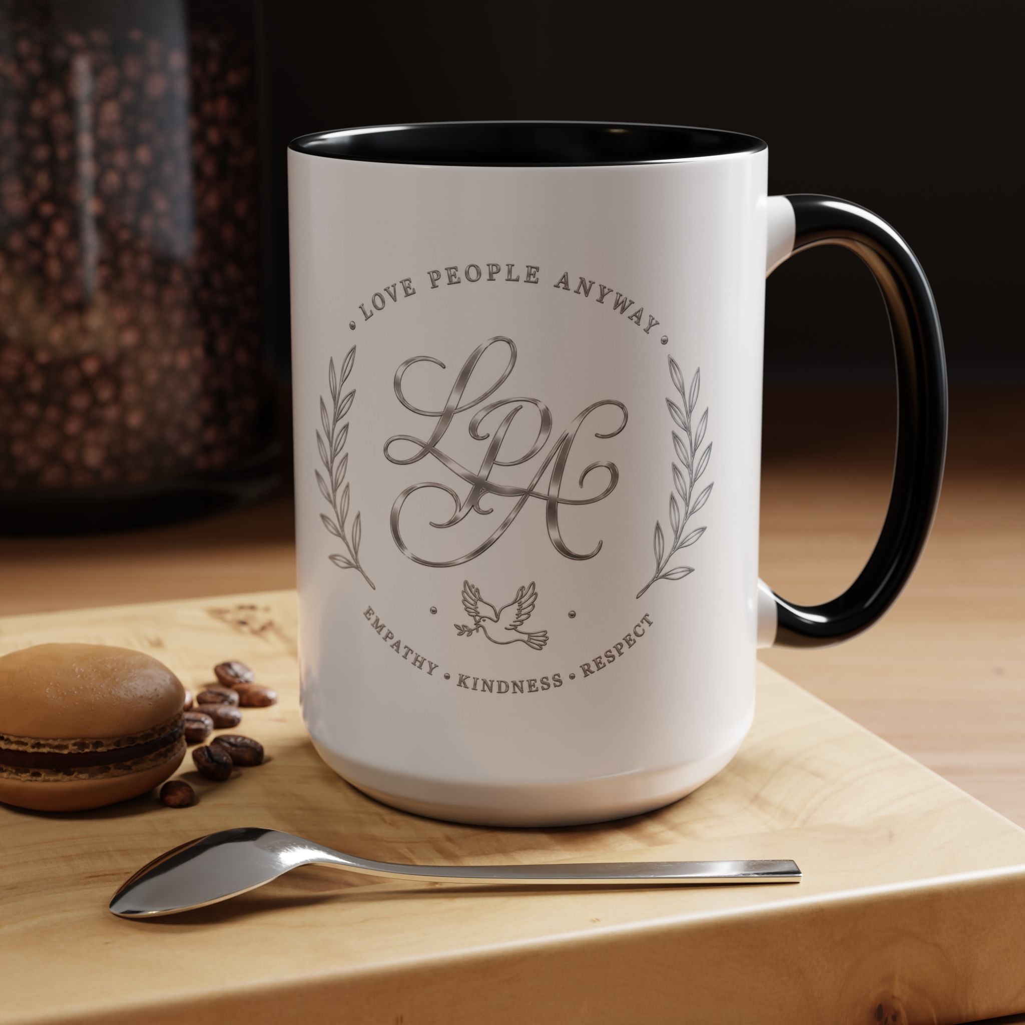 Inspirational ceramic coffee mug featuring silver “Love People Anyway” script, elegant monogram styling, decorative wreath accents, and contrasting handle and interior.