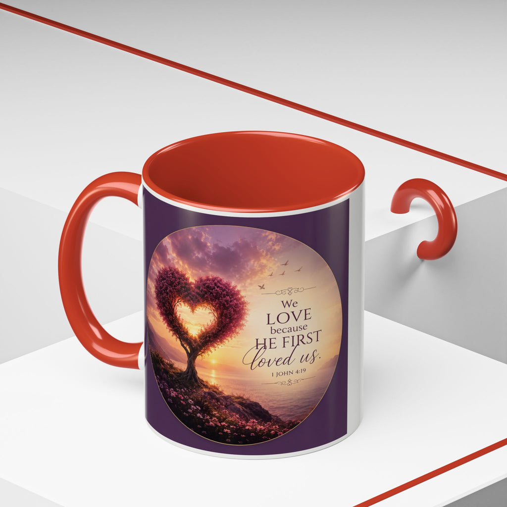 Inspirational Christian coffee mug featuring a glowing heart-shaped tree at sunset with the scripture “We Love Because He First Loved Us” from 1 John 4:19 and contrasting black handle and interior.