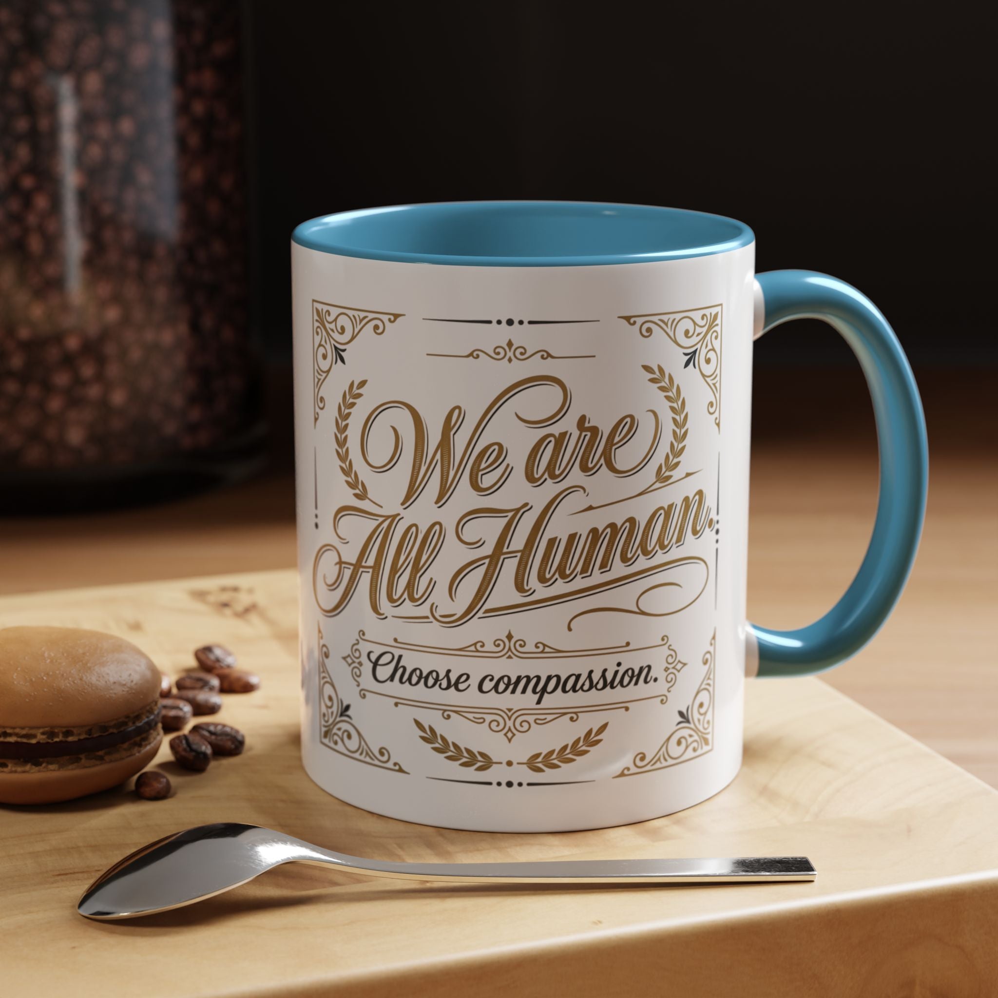 Inspirational ceramic accent coffee mug featuring “We Are All Human – Choose Compassion” in vintage-style gold lettering with decorative flourishes and black accent handle and interior.