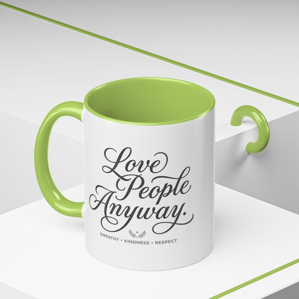 Inspirational ceramic accent coffee mug featuring hand-lettered “Love People Anyway” typography with empathy, kindness, and respect message on a glossy white mug with colorful handle and interior.
