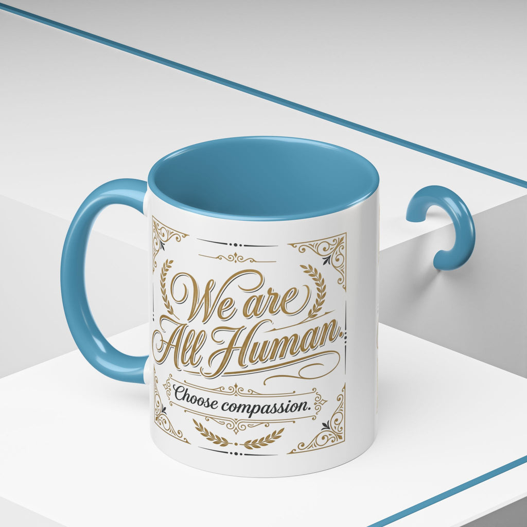 Inspirational ceramic accent coffee mug featuring “We Are All Human – Choose Compassion” in vintage-style gold lettering with decorative flourishes and black accent handle and interior.