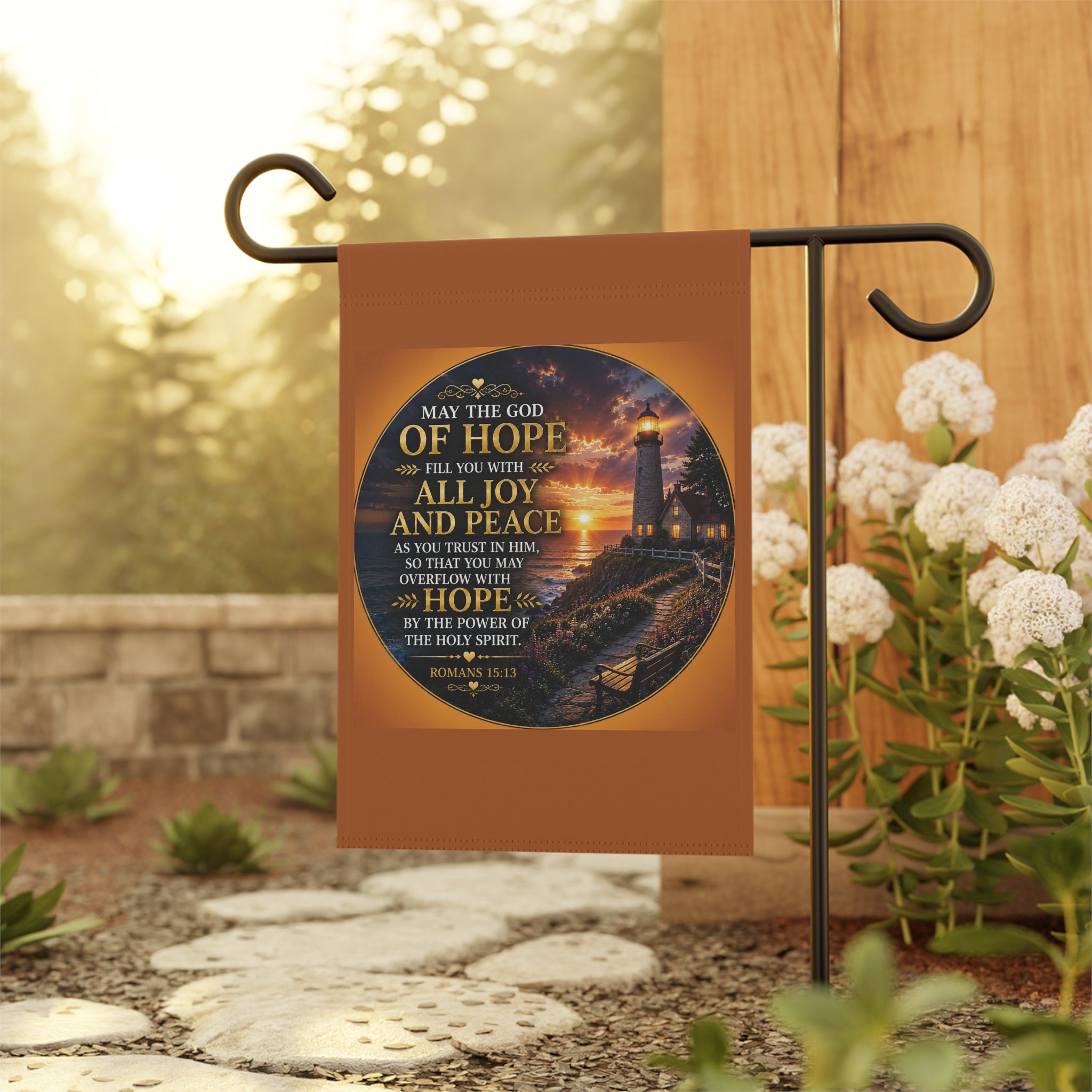 Inspirational Christian garden flag featuring a glowing lighthouse sunset with Romans 15:13 scripture artwork in warm coastal-inspired tones.