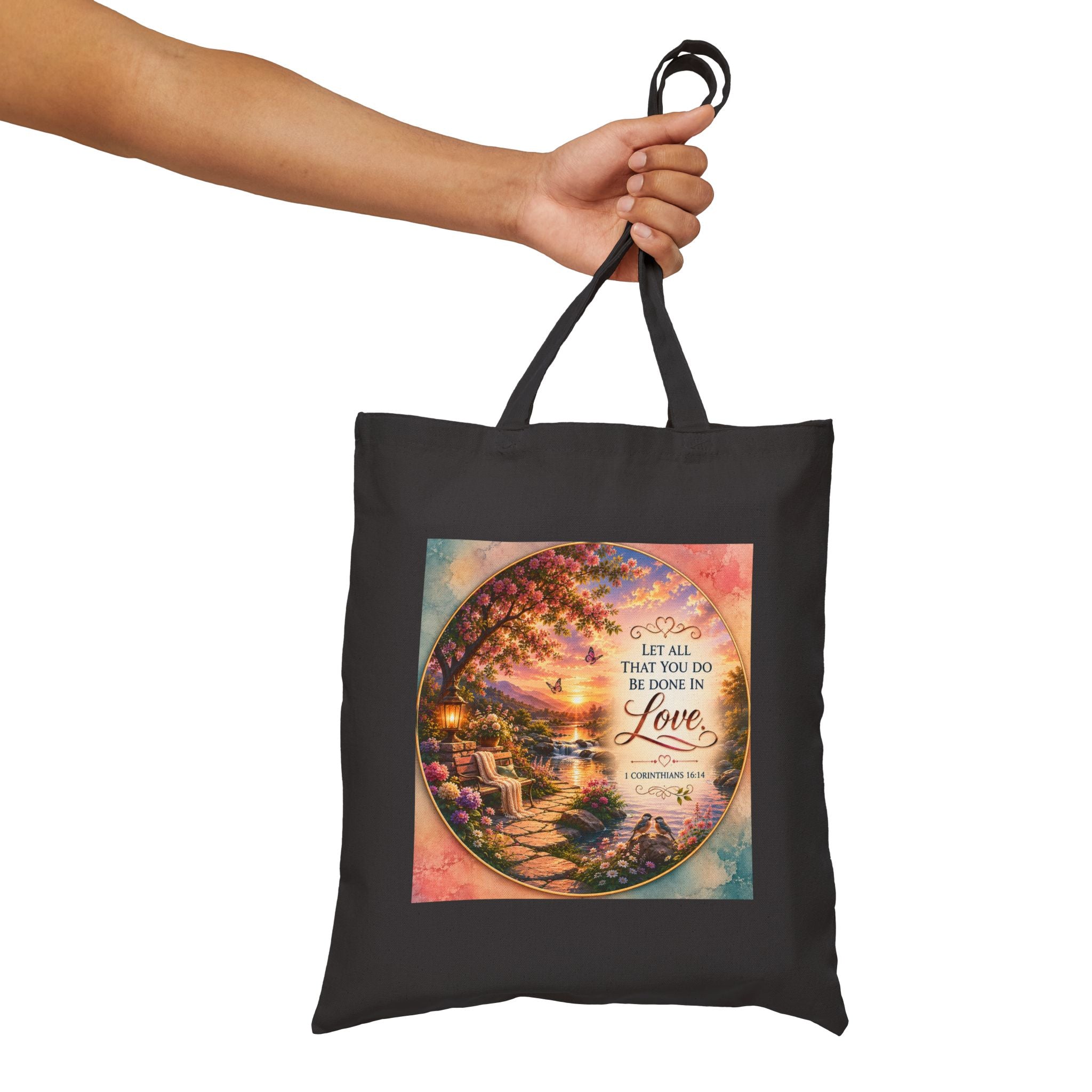 Christian cotton canvas tote bag featuring 1 Corinthians 16:14, “Let All That You Do Be Done in Love,” with a peaceful garden landscape, blooming flowers, butterflies, flowing river, lantern, birds, and sunset artwork.
