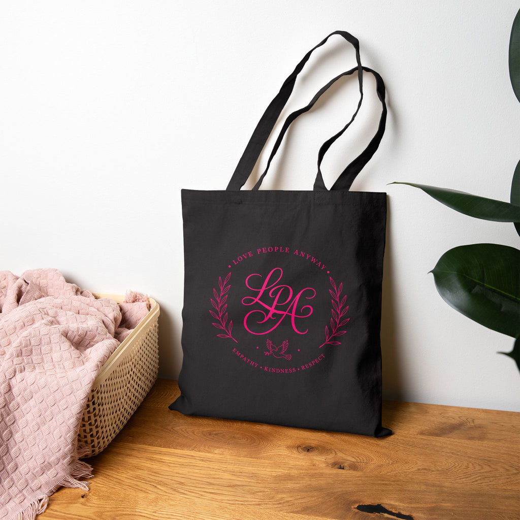 Pink monogram cotton canvas tote bag featuring the message “Love People Anyway,” laurel branches, a dove carrying an olive branch, and the words empathy, kindness, and respect in an elegant boutique design.