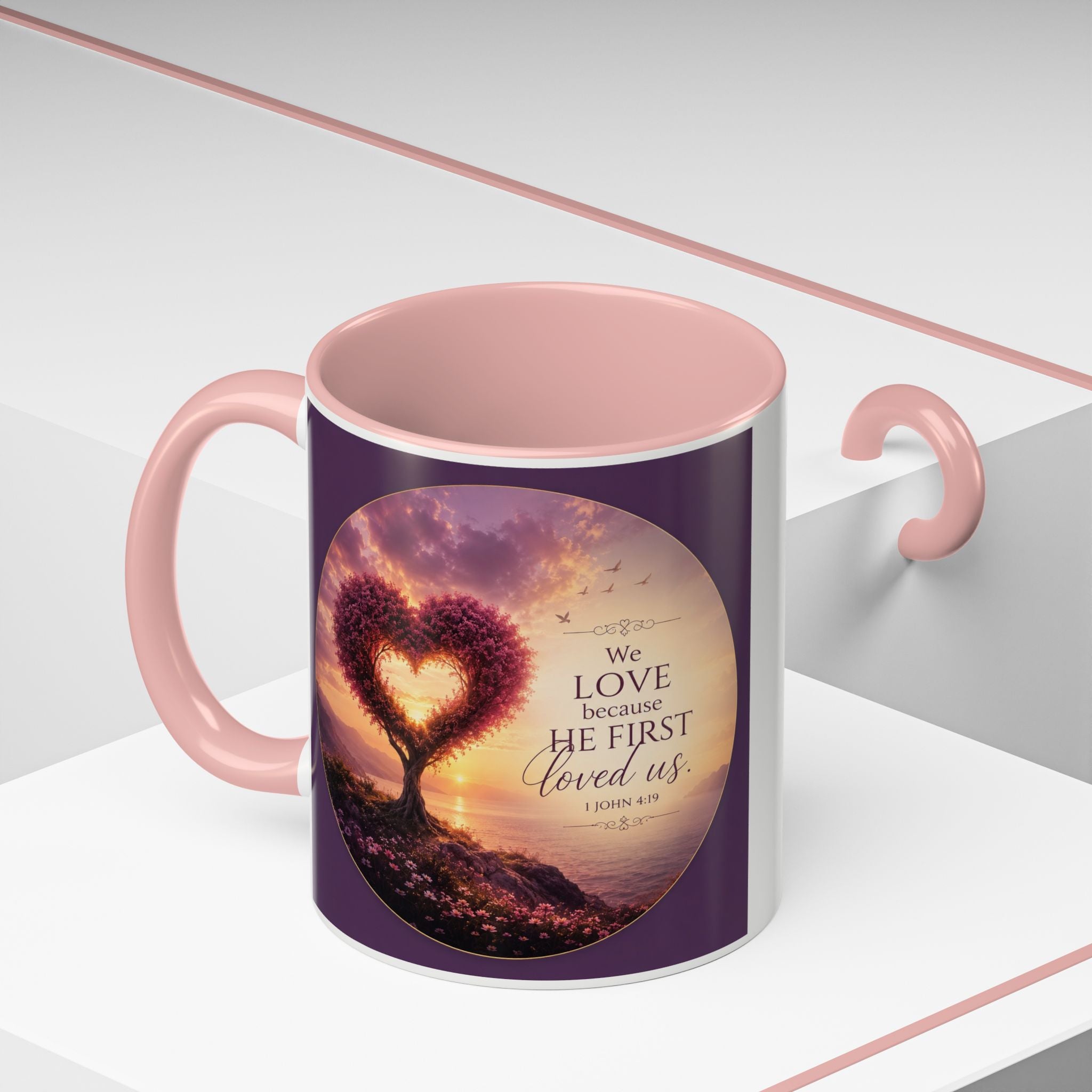 Inspirational Christian coffee mug featuring a glowing heart-shaped tree at sunset with the scripture “We Love Because He First Loved Us” from 1 John 4:19 and contrasting black handle and interior.