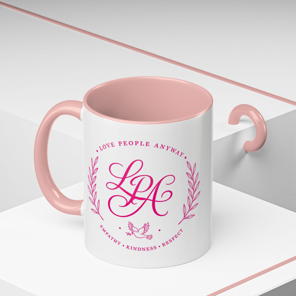 Inspirational ceramic coffee mug featuring soft pink “Love People Anyway” lettering, laurel accents, a dove motif, and contrasting black handle and interior.
