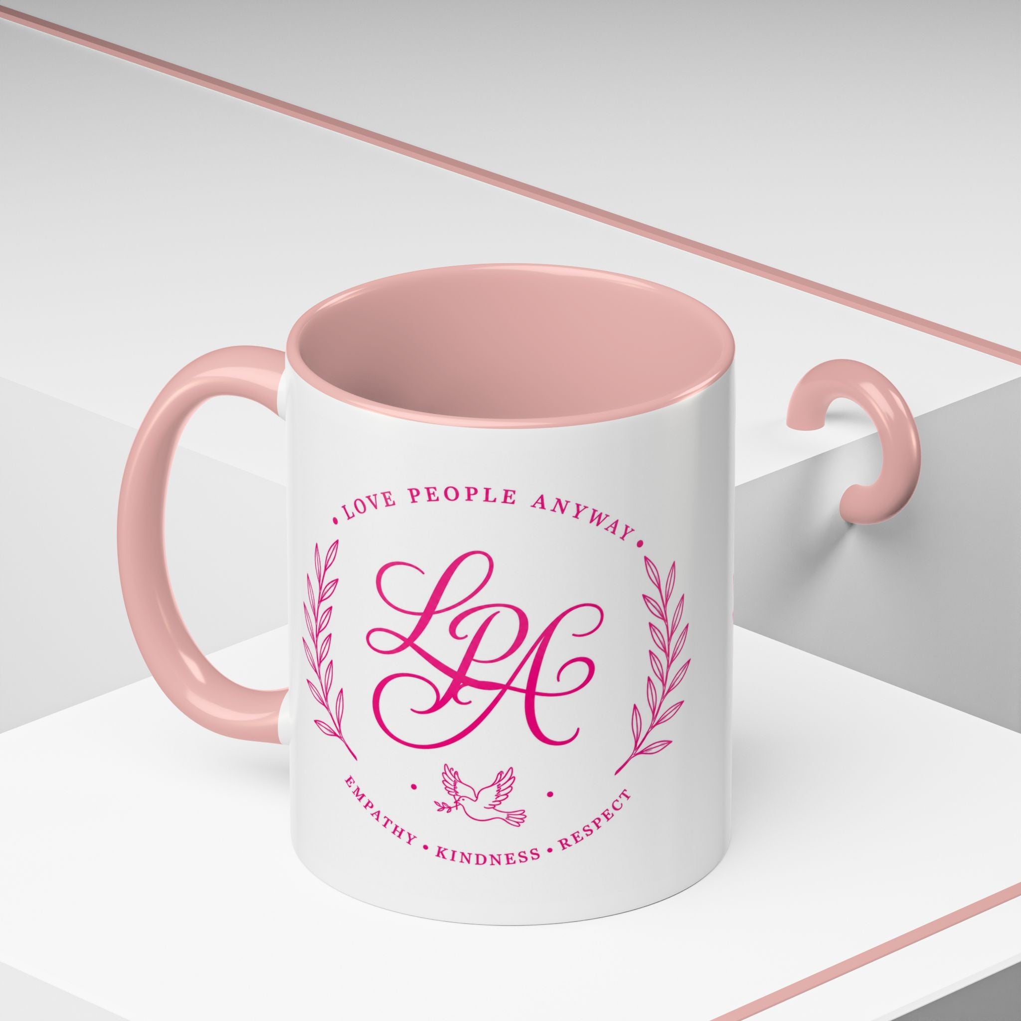 Inspirational ceramic coffee mug featuring soft pink “Love People Anyway” lettering, laurel accents, a dove motif, and contrasting black handle and interior.