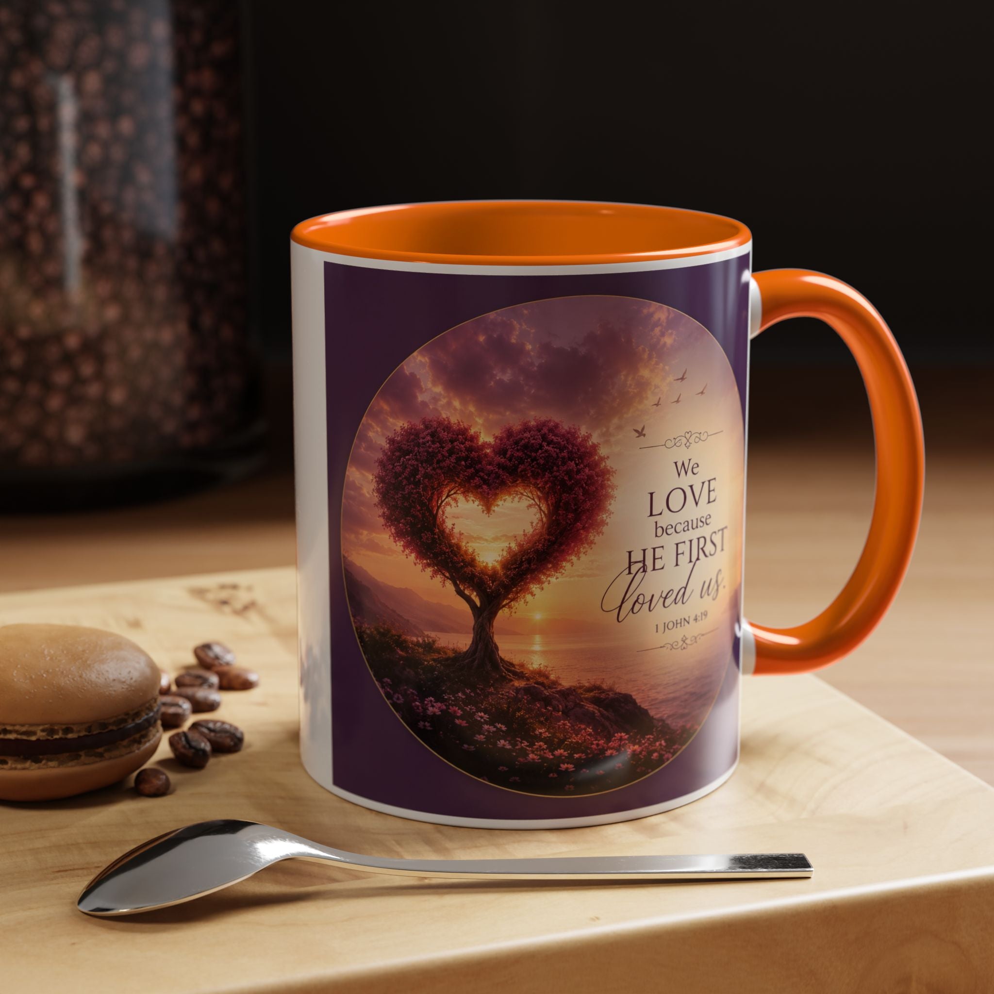 Inspirational Christian coffee mug featuring a glowing heart-shaped tree at sunset with the scripture “We Love Because He First Loved Us” from 1 John 4:19 and contrasting black handle and interior.