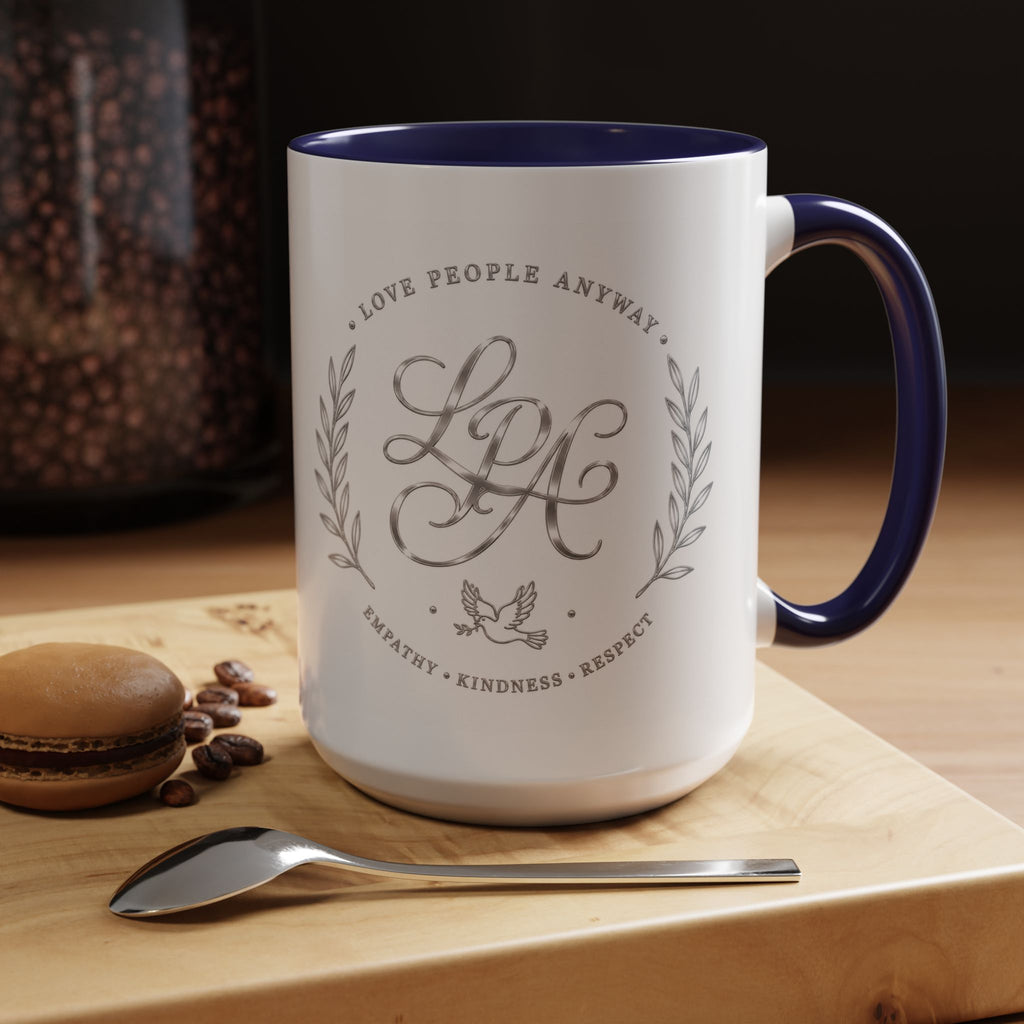 Inspirational ceramic coffee mug featuring silver “Love People Anyway” script, elegant monogram styling, decorative wreath accents, and contrasting handle and interior.