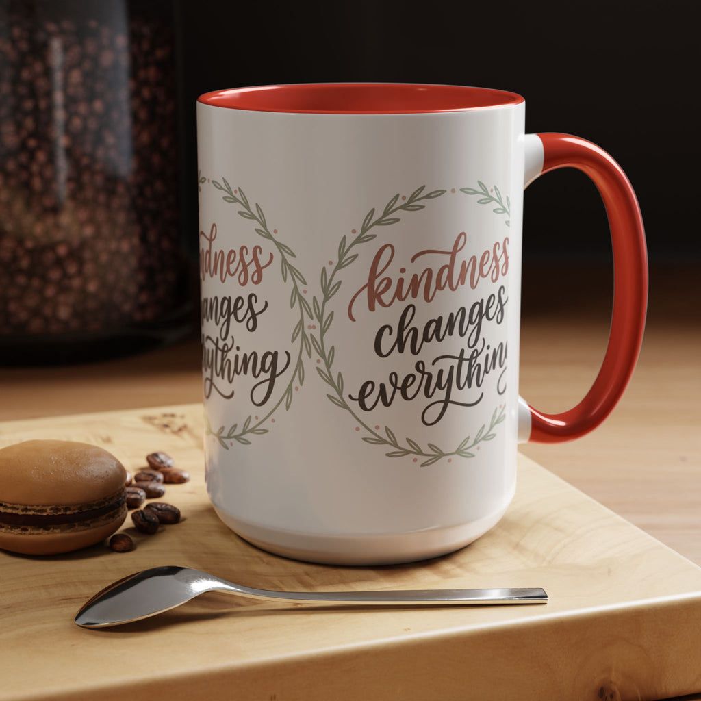 Inspirational ceramic accent coffee mug featuring hand-lettered “Kindness Changes Everything” typography surrounded by a delicate laurel wreath in soft sage and blush tones.