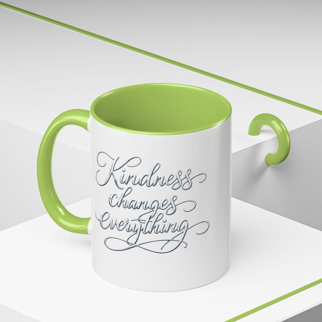 Inspirational ceramic accent coffee mug featuring elegant silver hand-lettered “Kindness Changes Everything” typography with colorful handle and interior accents.