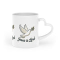 White ceramic heart-shaped handle mug featuring repeating white doves carrying olive branches with the words "Jesus Is Lord" in elegant script.