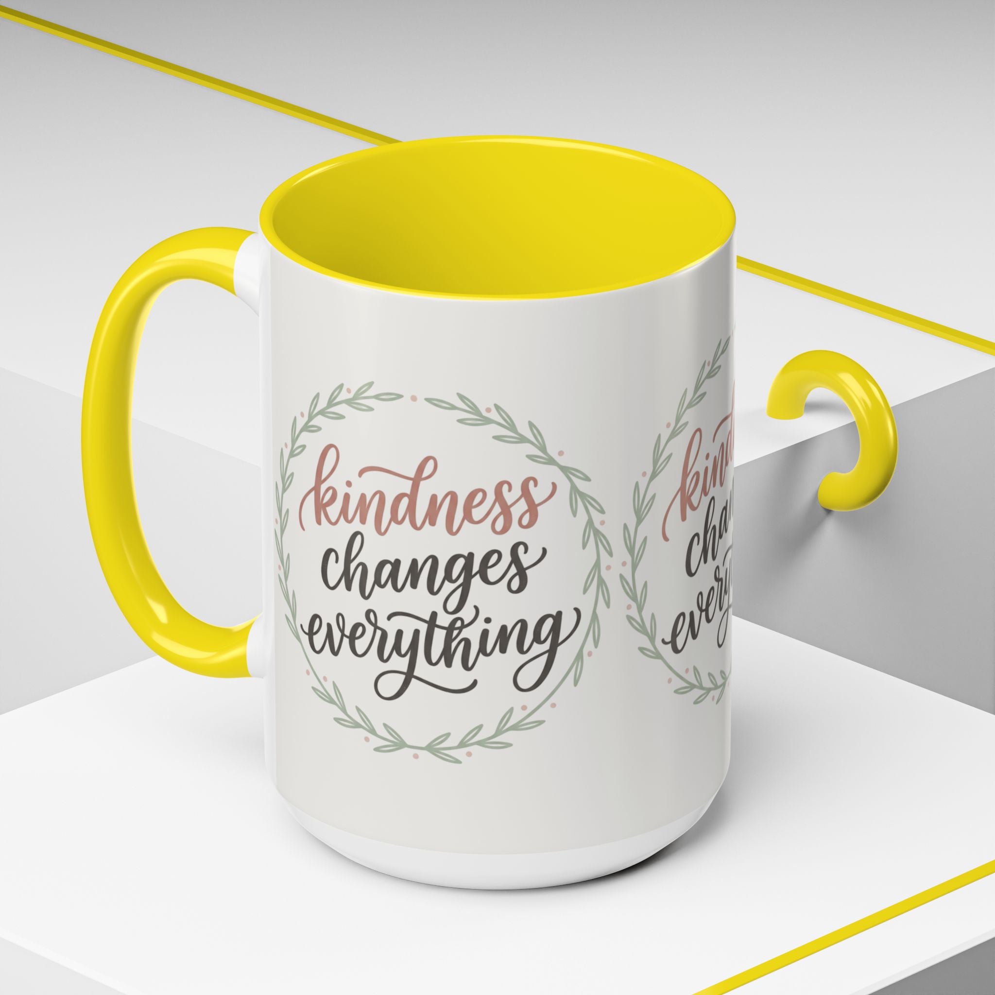 Inspirational ceramic accent coffee mug featuring hand-lettered “Kindness Changes Everything” typography surrounded by a delicate laurel wreath in soft sage and blush tones.