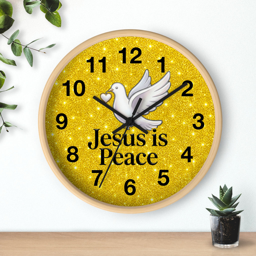 A round wall clock with a light wood frame and a glittery gold face. The clock features a white dove in the center, black Arabic numerals, black hands, and the text 'Jesus is Peace' in black.