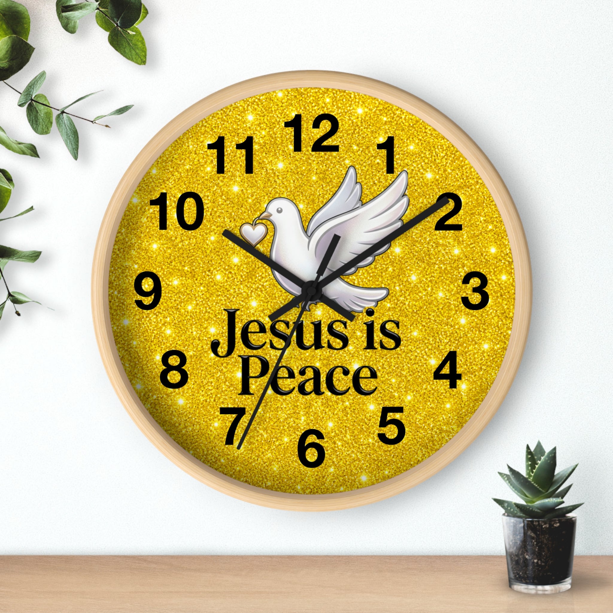 A round wall clock with a light wood frame and a glittery gold face. The clock features a white dove in the center, black Arabic numerals, black hands, and the text 'Jesus is Peace' in black.