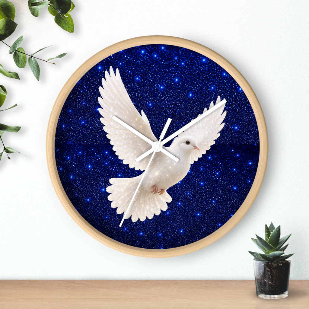 Round wall clock with a light wood frame, featuring a white dove in flight over a deep blue starry night background. The clock is mounted on a white wall above a wooden surface with a small potted succulent and green leaves in the corners.