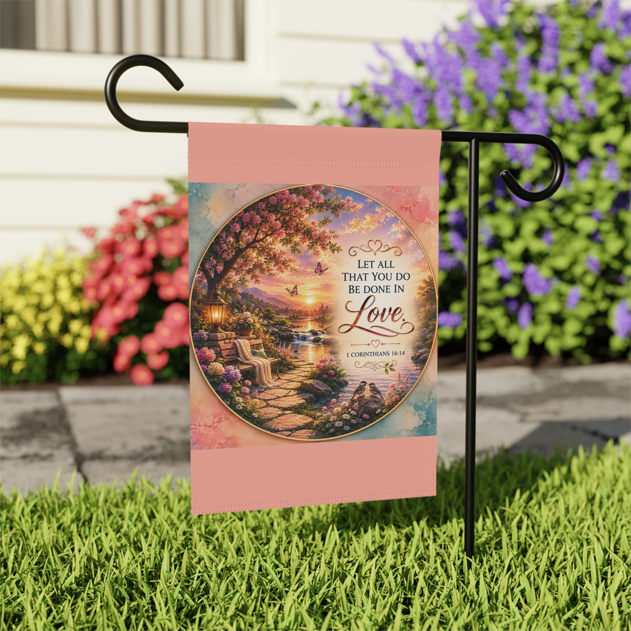 Inspirational Christian garden flag featuring a lantern-lit waterfront pathway, blooming flowers, and the scripture “Let All That You Do Be Done in Love” in warm sunset tones.
