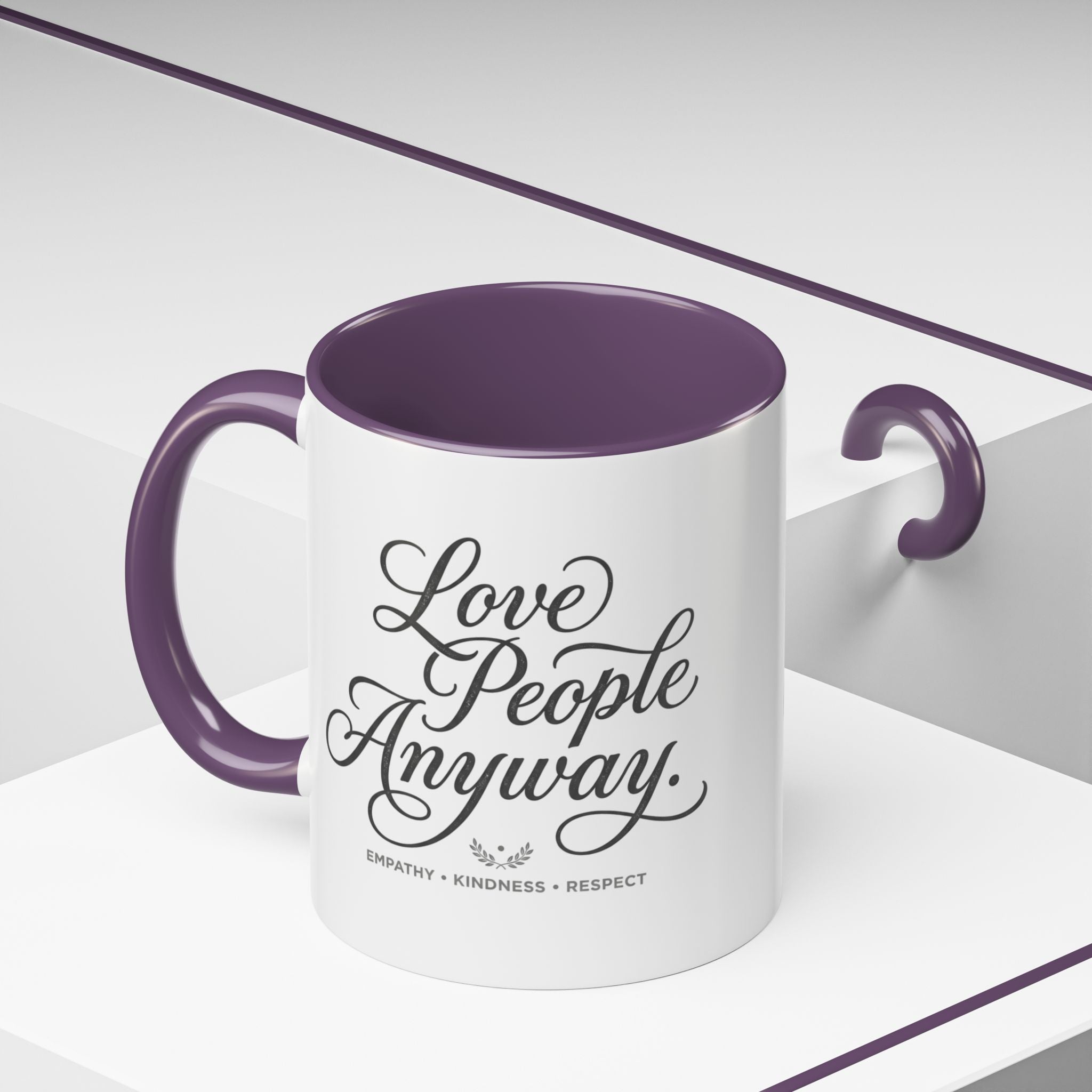Inspirational ceramic accent coffee mug featuring hand-lettered “Love People Anyway” typography with empathy, kindness, and respect message on a glossy white mug with colorful handle and interior.