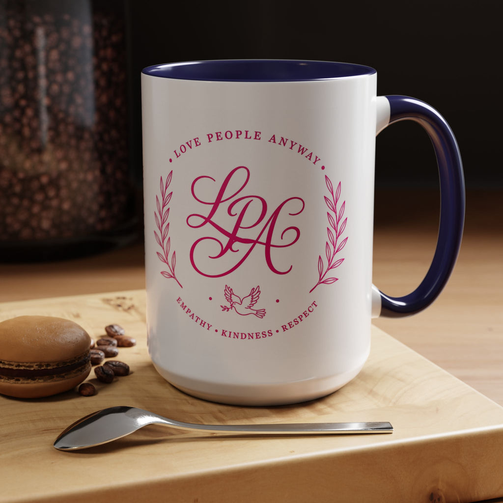 Inspirational ceramic coffee mug featuring soft pink “Love People Anyway” lettering, laurel accents, a dove motif, and contrasting purple handle and interior.