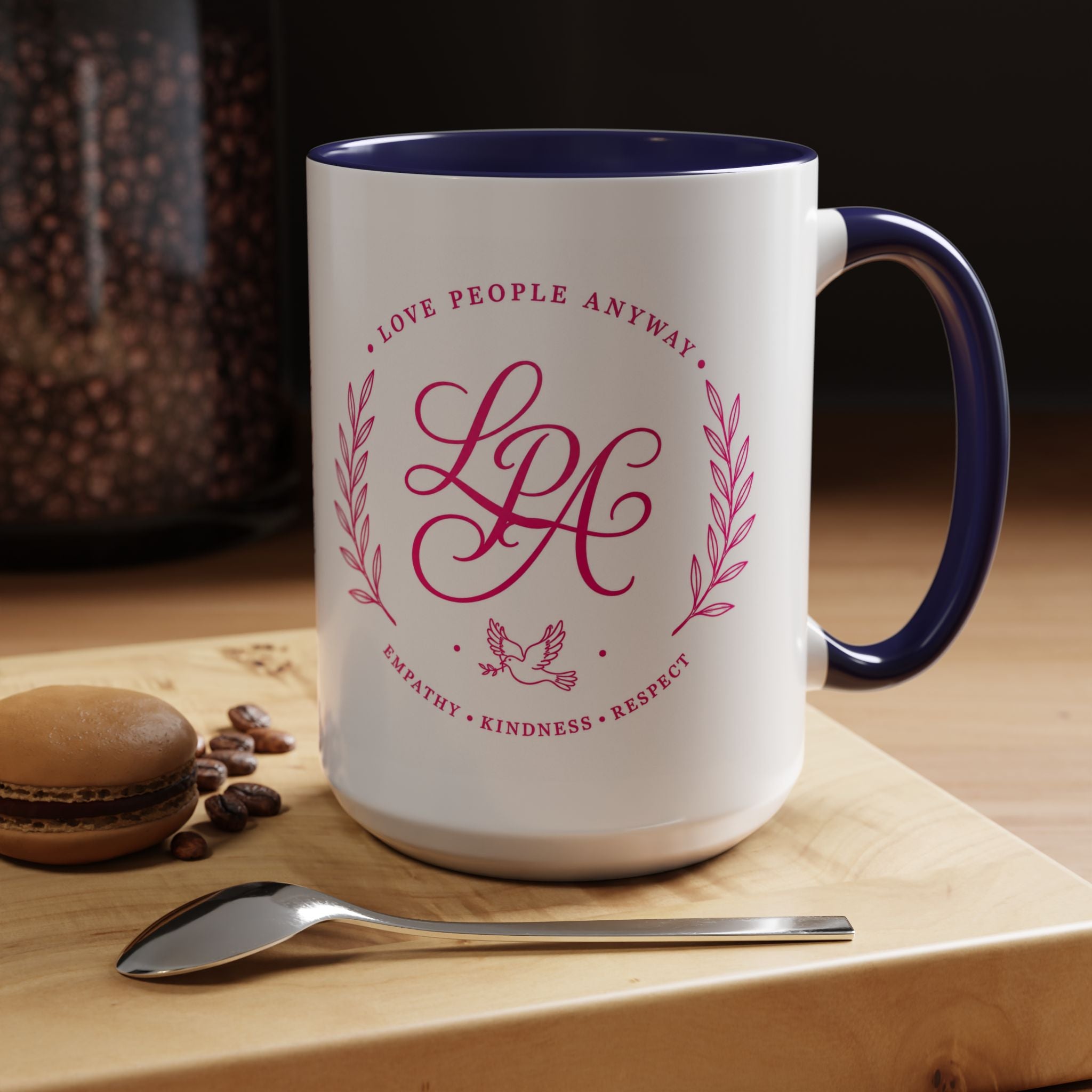 Inspirational ceramic coffee mug featuring soft pink “Love People Anyway” lettering, laurel accents, a dove motif, and contrasting purple handle and interior.