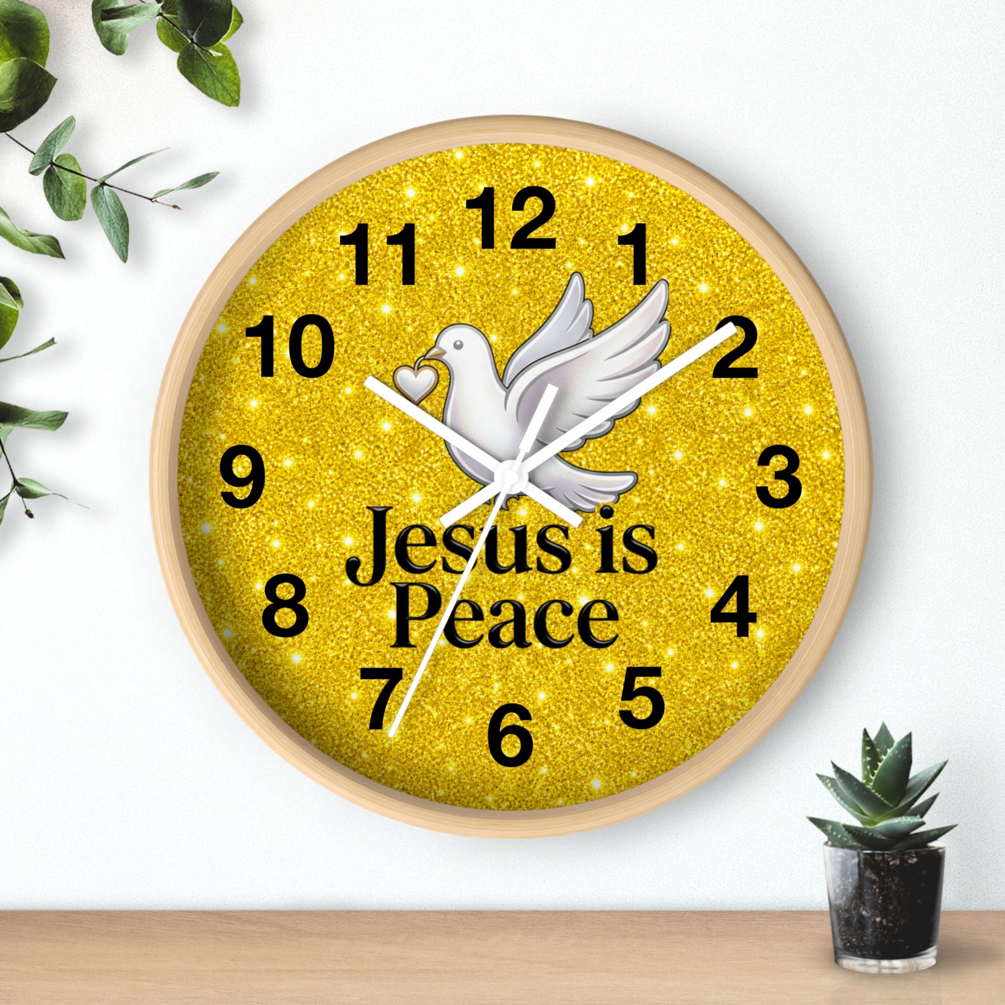 A round wall clock with a light wood frame and a glittery gold face. The clock features a white dove in the center, black Arabic numerals, white hands, and the text 'Jesus is Peace' in black.