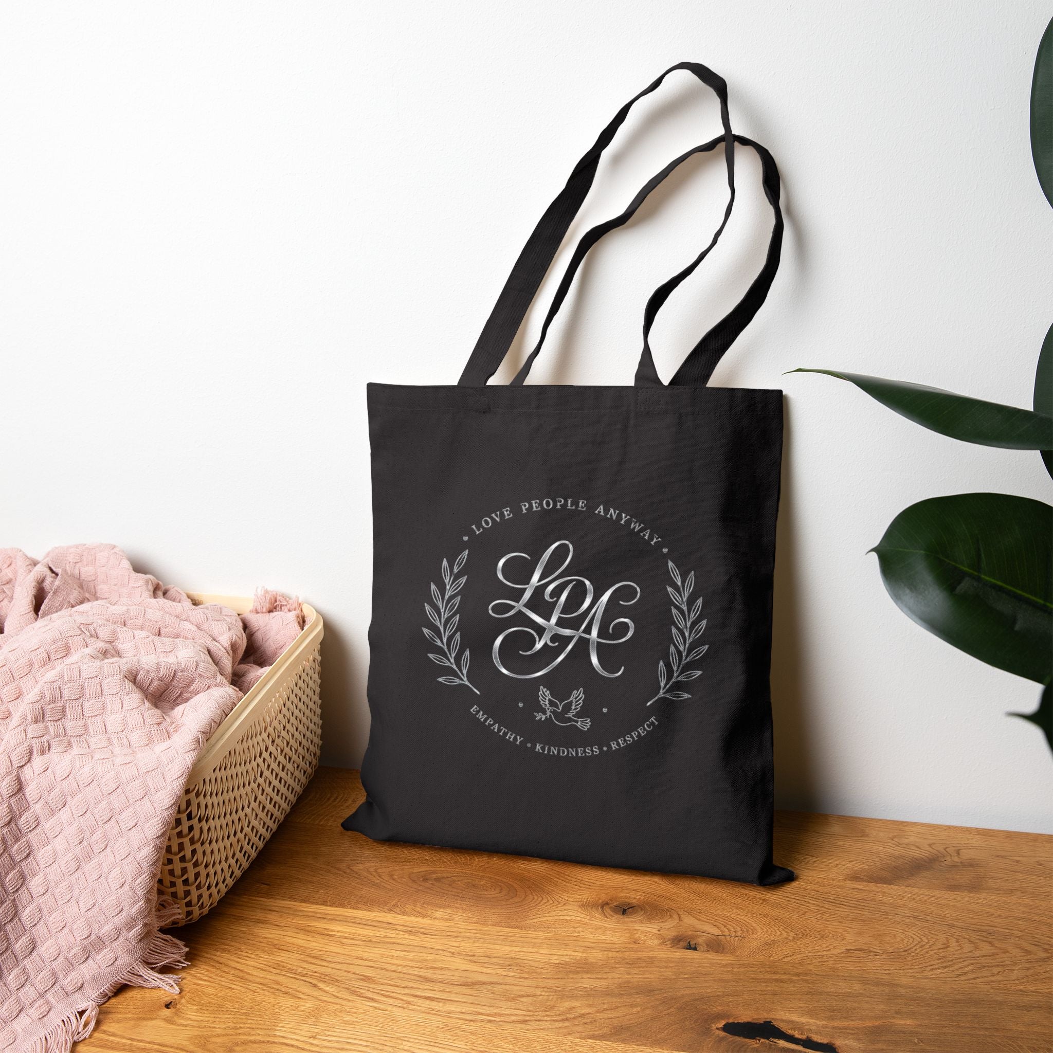 Elegant cotton canvas tote bag featuring a silver monogram crest, laurel branches, dove with olive branch, and the message “Love People Anyway” with empathy, kindness, and respect accents.