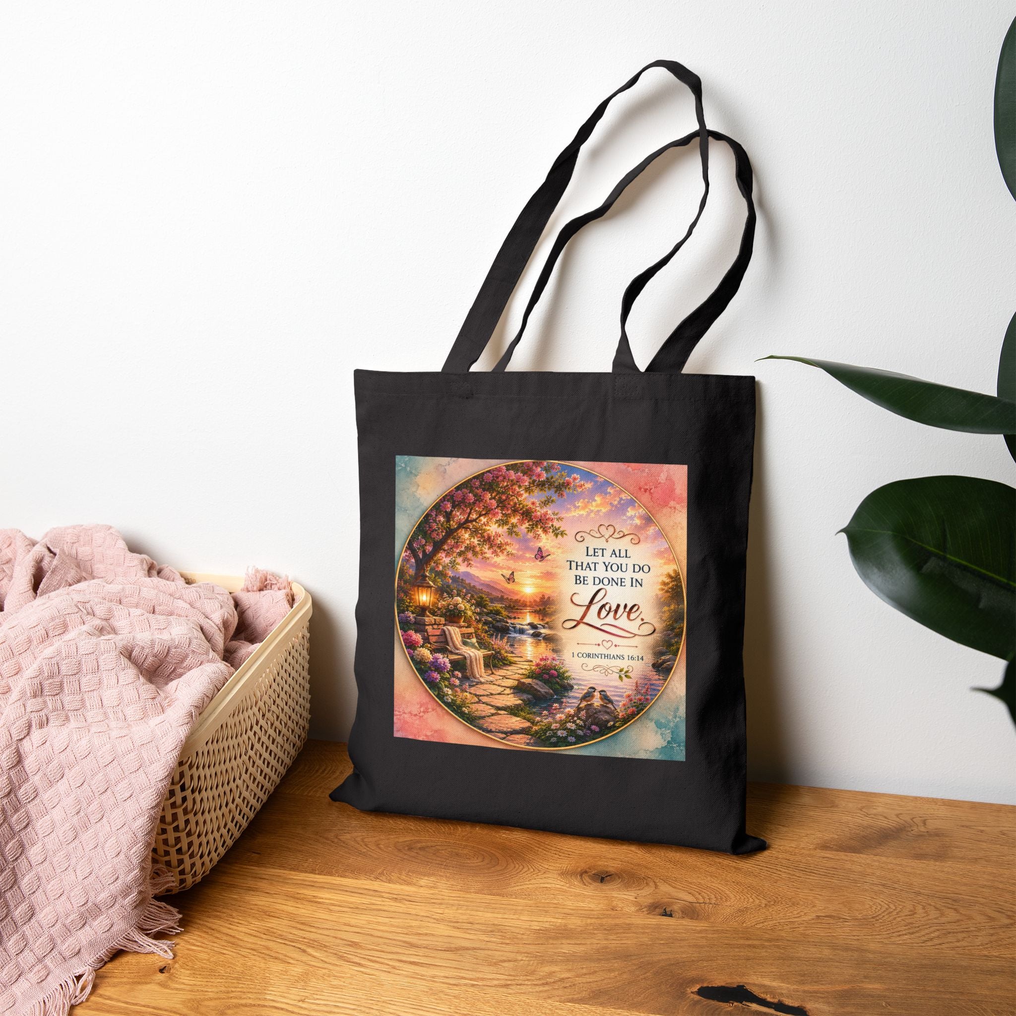 Christian cotton canvas tote bag featuring 1 Corinthians 16:14, “Let All That You Do Be Done in Love,” with a peaceful garden landscape, blooming flowers, butterflies, flowing river, lantern, birds, and sunset artwork.
