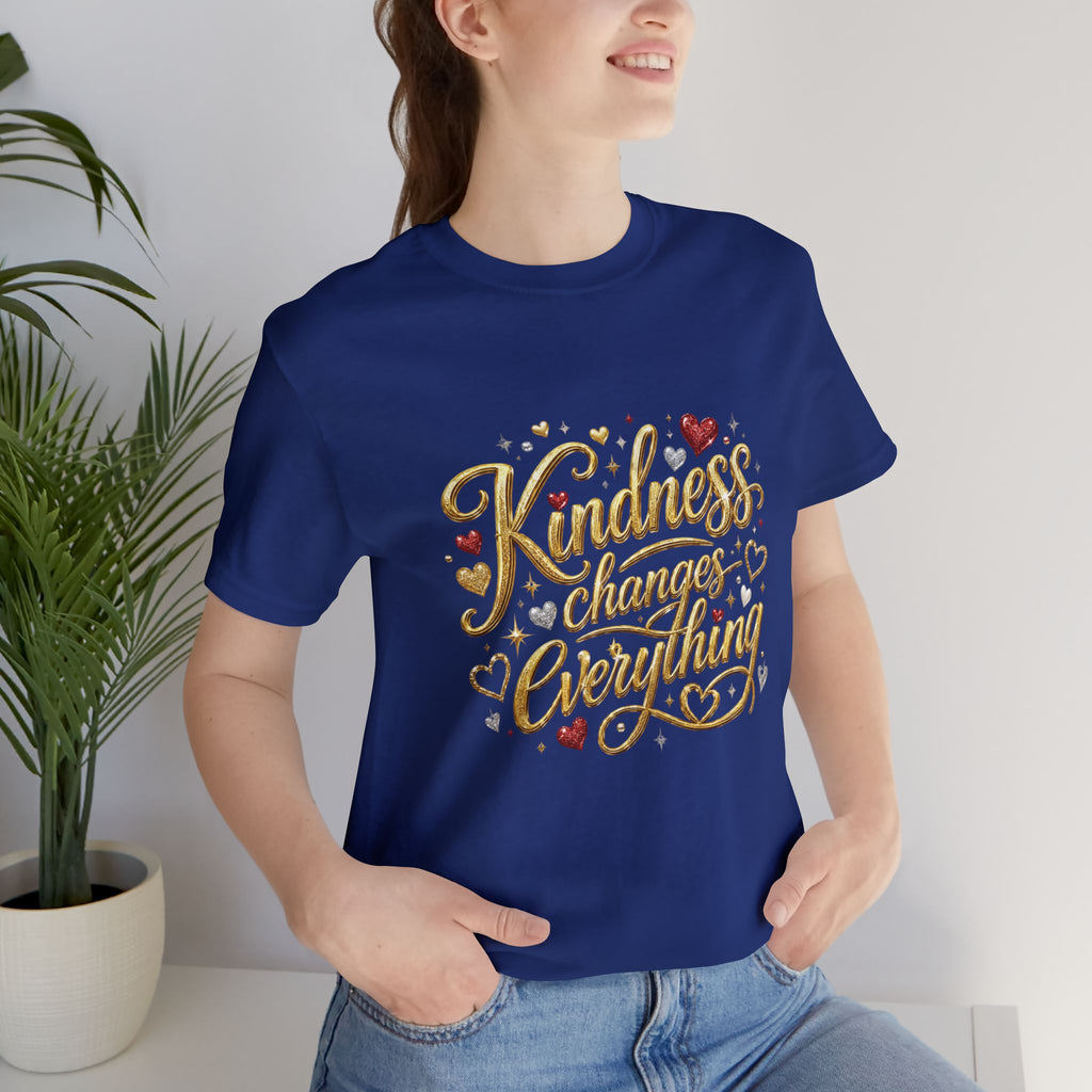Inspirational t-shirt featuring gold script reading “Kindness Changes Everything” with subtle heart accents and a small heart embrace illustration on the upper back.