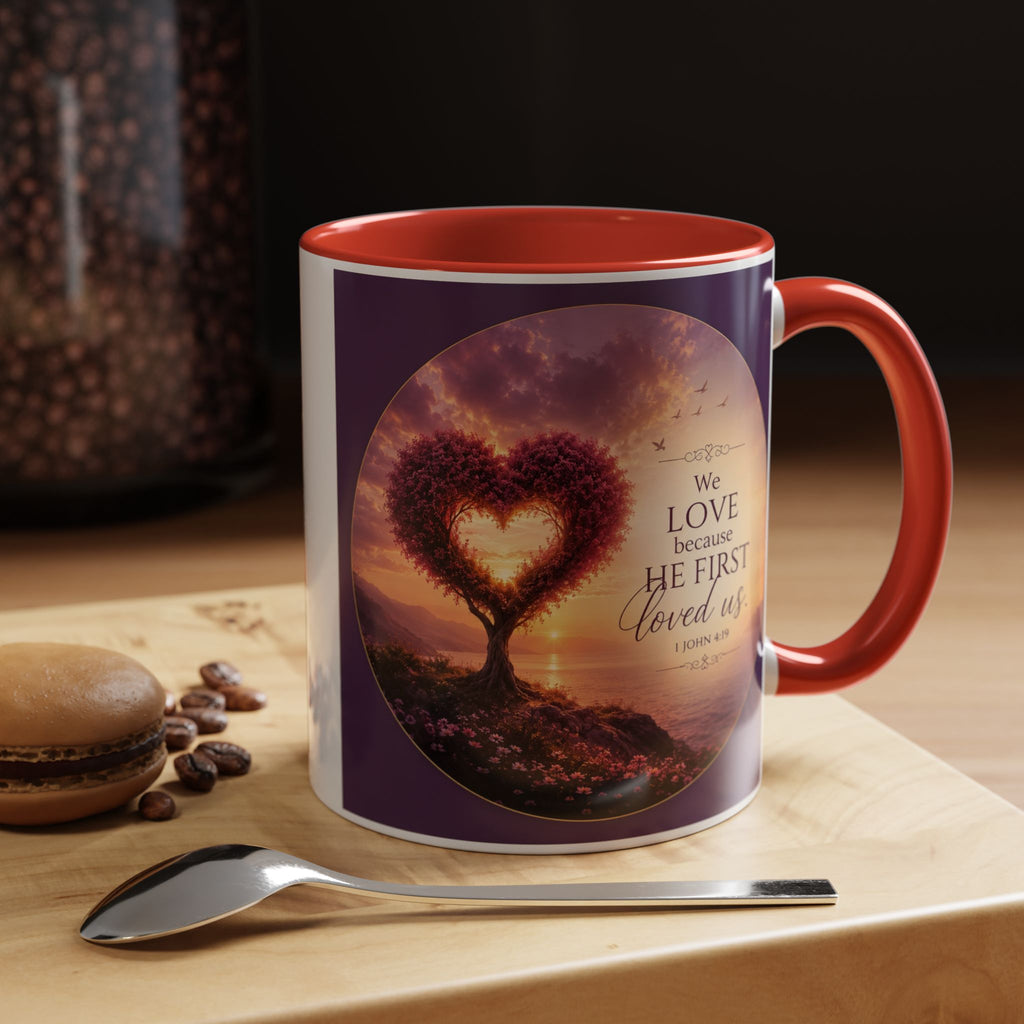 Inspirational Christian coffee mug featuring a glowing heart-shaped tree at sunset with the scripture “We Love Because He First Loved Us” from 1 John 4:19 and contrasting black handle and interior.