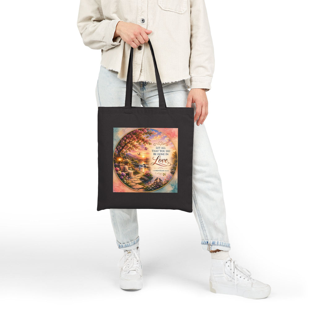 Christian cotton canvas tote bag featuring 1 Corinthians 16:14, “Let All That You Do Be Done in Love,” with a peaceful garden landscape, blooming flowers, butterflies, flowing river, lantern, birds, and sunset artwork.