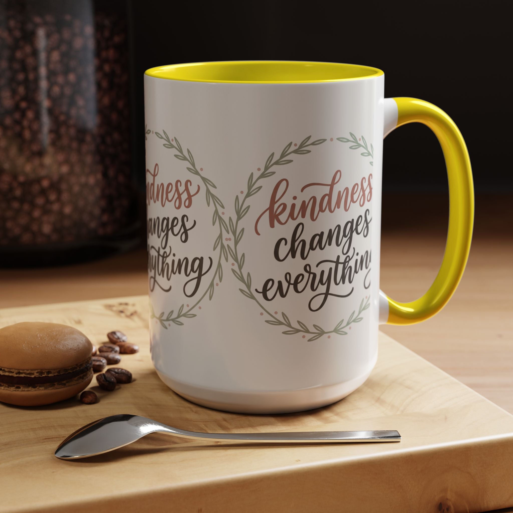Inspirational ceramic accent coffee mug featuring hand-lettered “Kindness Changes Everything” typography surrounded by a delicate laurel wreath in soft sage and blush tones.