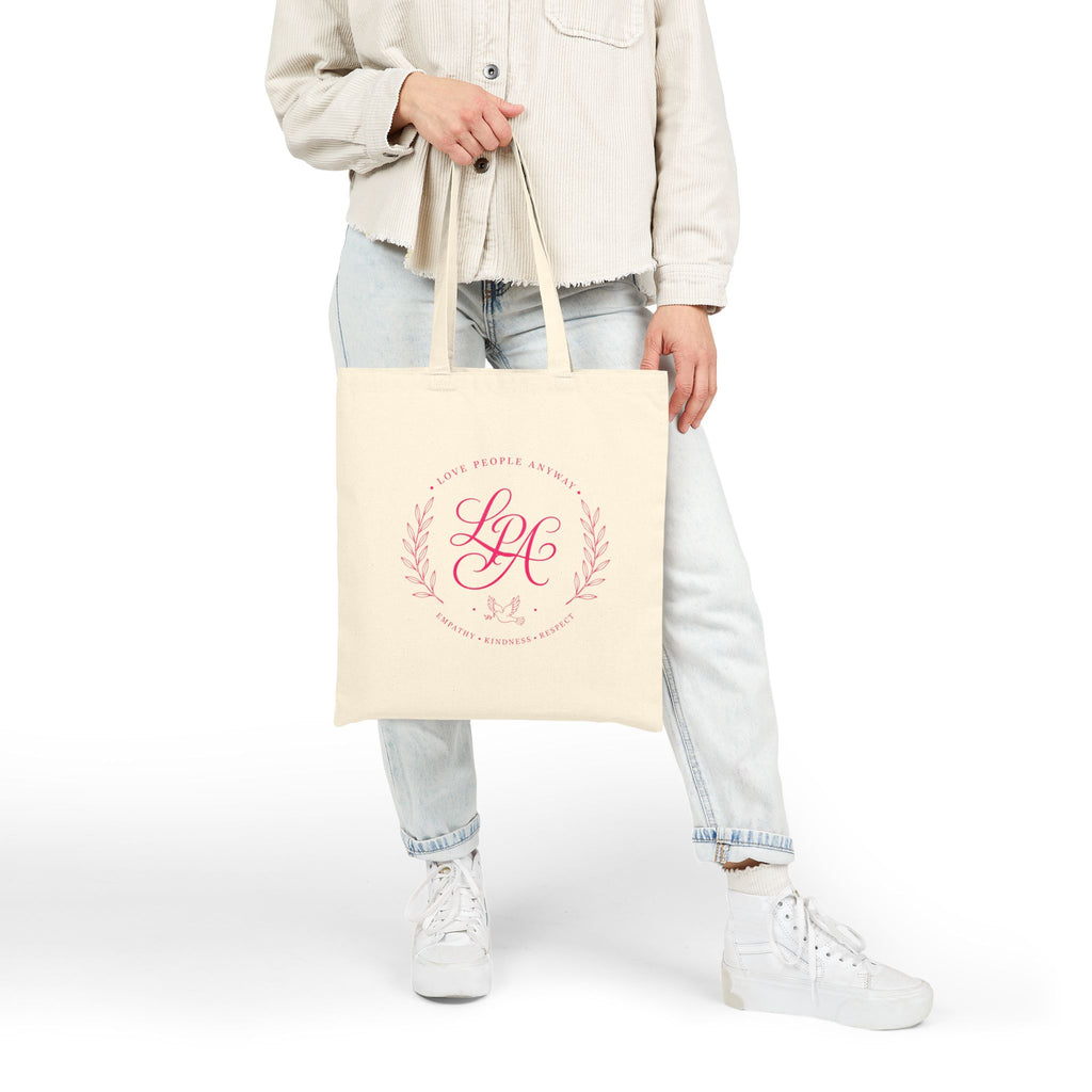 Pink monogram cotton canvas tote bag featuring the message “Love People Anyway,” laurel branches, a dove carrying an olive branch, and the words empathy, kindness, and respect in an elegant boutique design.