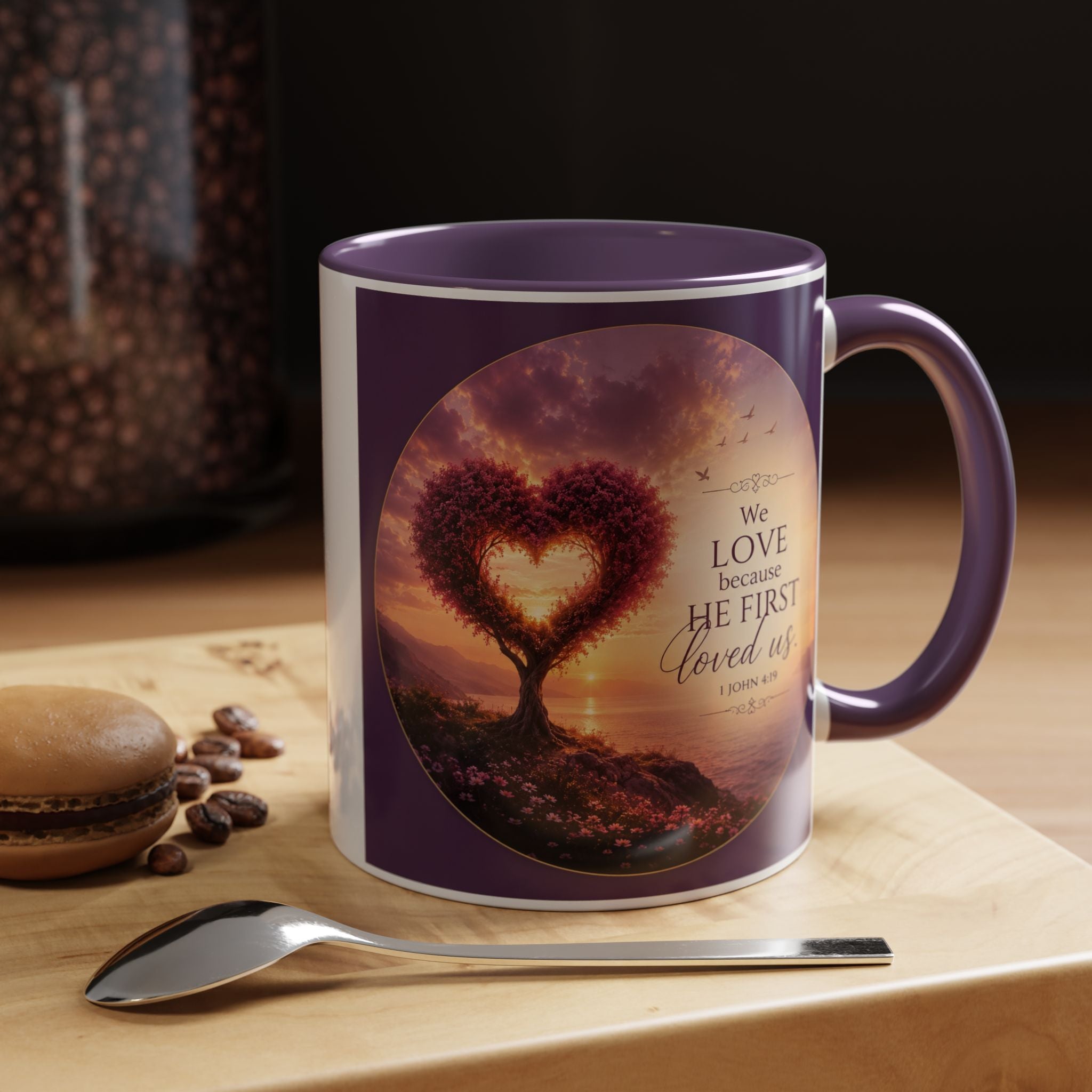 Inspirational Christian coffee mug featuring a glowing heart-shaped tree at sunset with the scripture “We Love Because He First Loved Us” from 1 John 4:19 and contrasting black handle and interior.