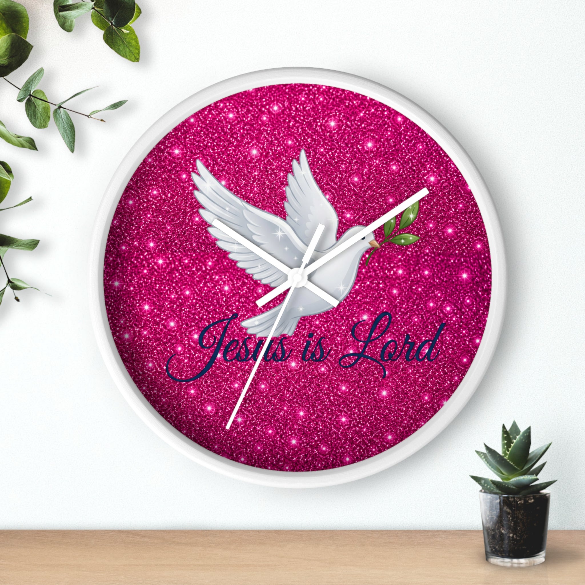 Round wall clock featuring a white dove carrying an olive branch with the words "Jesus Is Lord" on a sparkling pink background, finished with a wood frame and silent quartz movement.