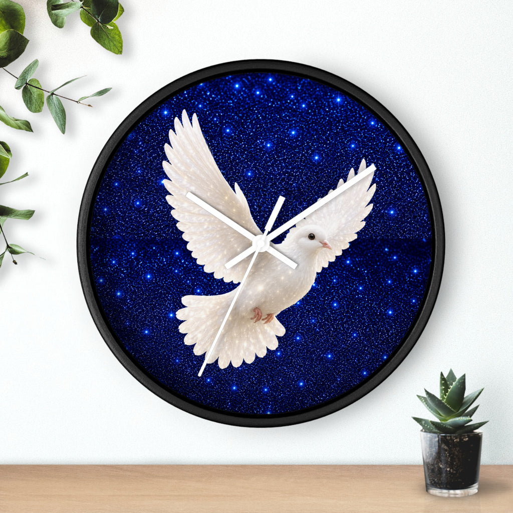 Round wall clock with a black frame, featuring a white dove in flight over a deep blue starry night background. The clock is mounted on a white wall above a light wood surface, with decorative green leaves and a small potted succulent nearby.