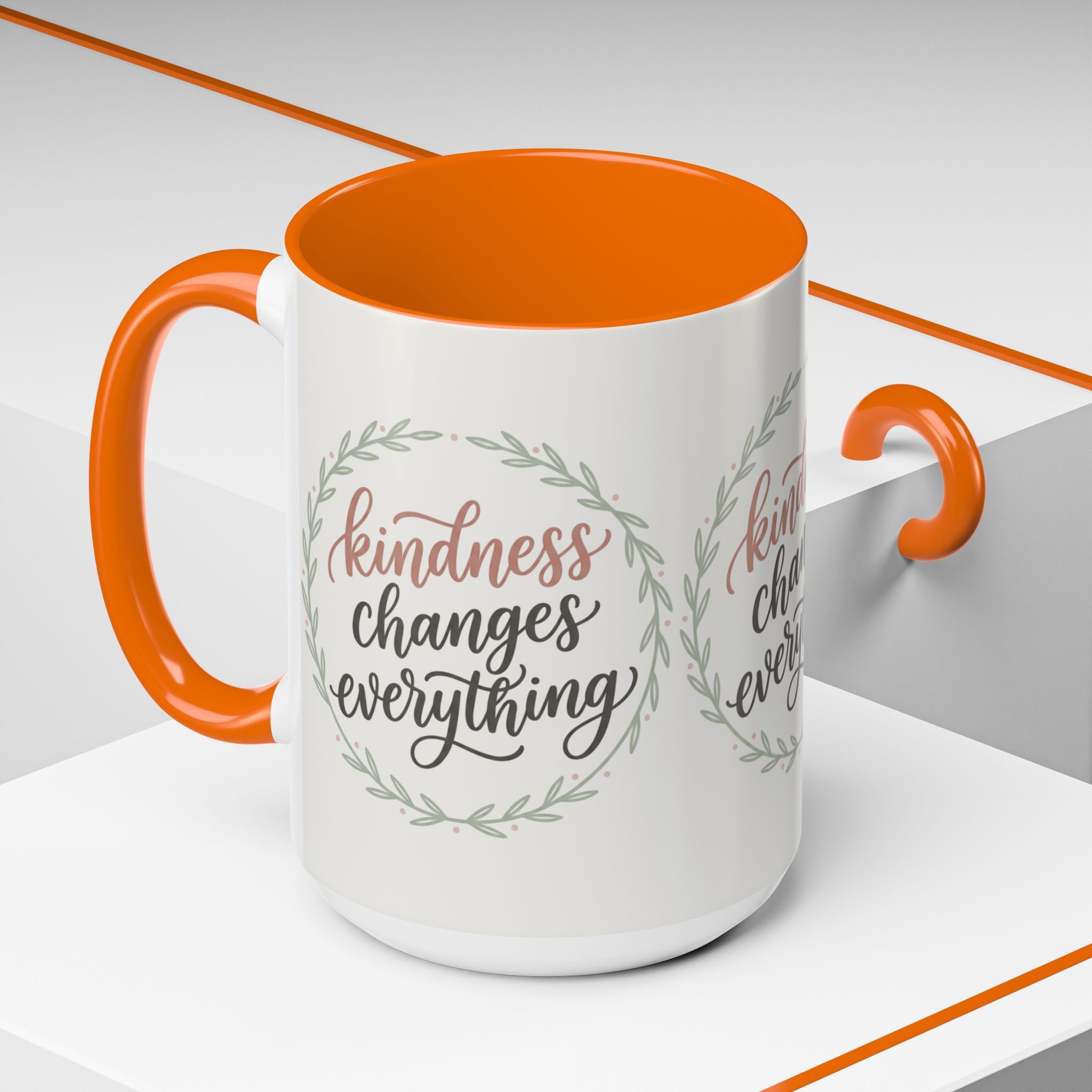 Inspirational ceramic accent coffee mug featuring hand-lettered “Kindness Changes Everything” typography surrounded by a delicate laurel wreath in soft sage and blush tones.