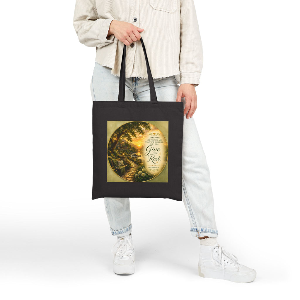 Christian cotton canvas tote bag featuring Matthew 11:28, “Come to Me, all you who are weary and burdened, and I will give you rest,” with peaceful garden pathway, glowing lanterns, riverside cottages, blooming flowers, and sunset artwork.