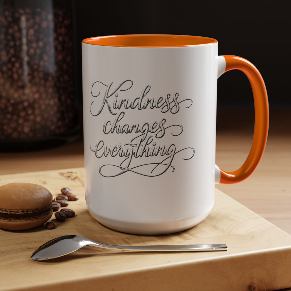 Inspirational ceramic accent coffee mug featuring elegant silver hand-lettered “Kindness Changes Everything” typography with colorful handle and interior accents.