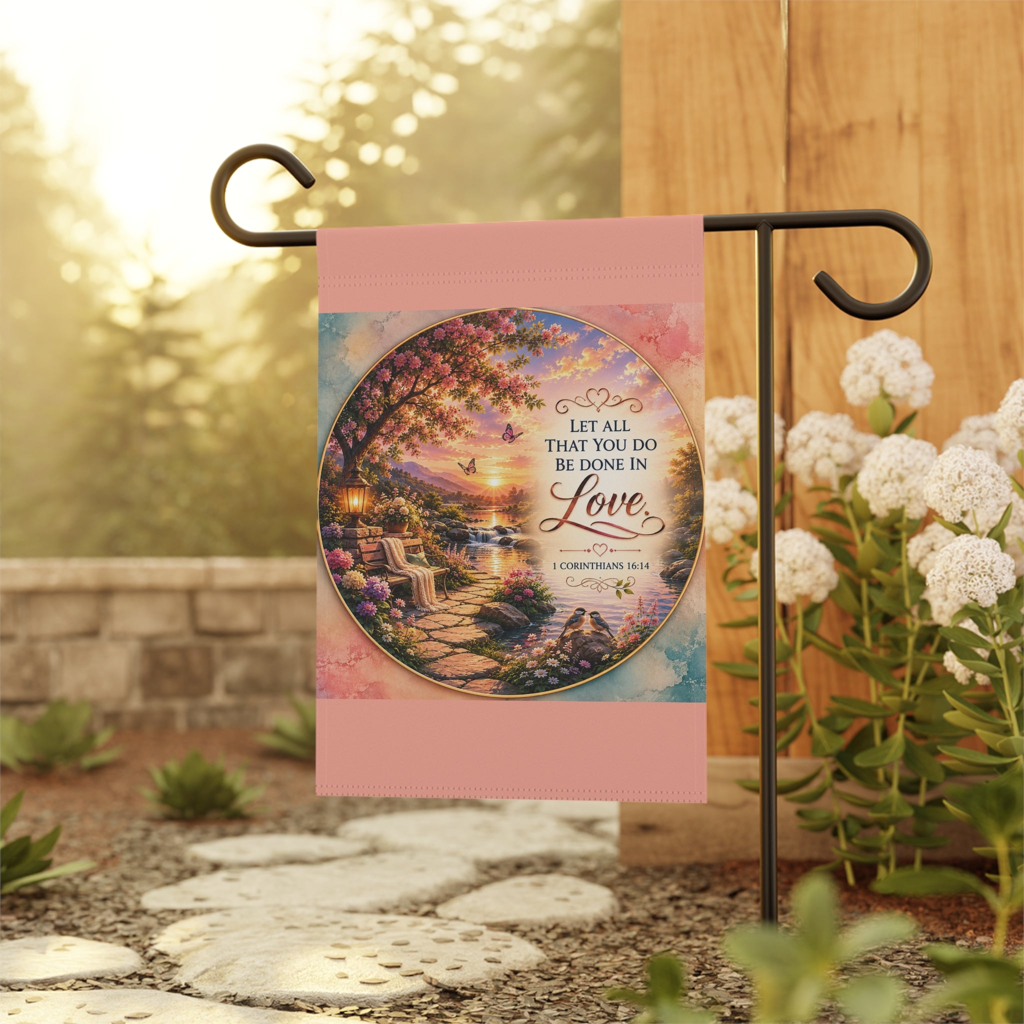Inspirational Christian garden flag featuring a lantern-lit waterfront pathway, blooming flowers, and the scripture “Let All That You Do Be Done in Love” in warm sunset tones.