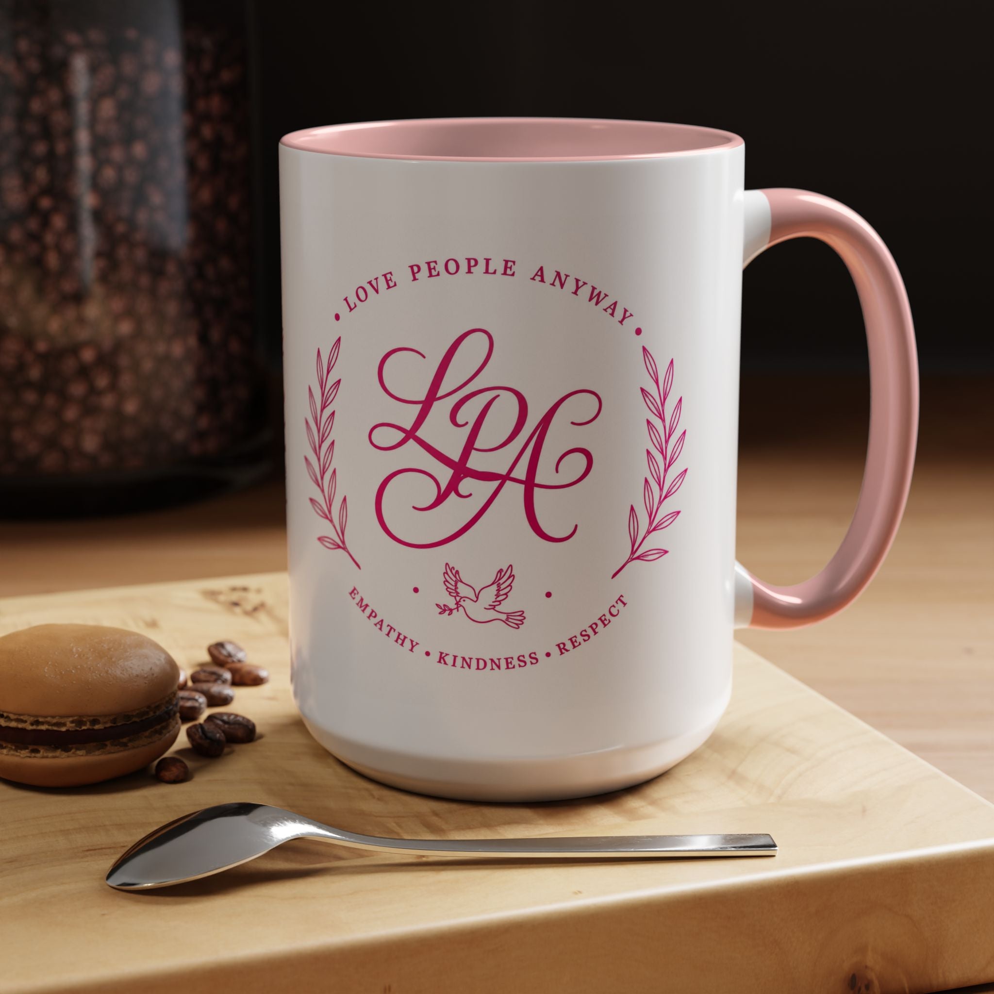 Inspirational ceramic coffee mug featuring soft pink “Love People Anyway” lettering, laurel accents, a dove motif, and contrasting pink handle and interior.