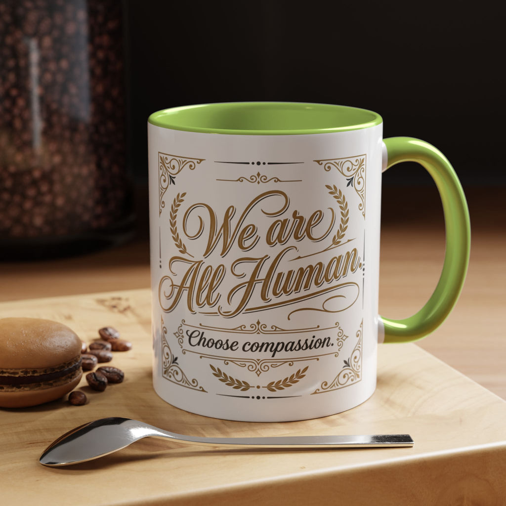 Inspirational ceramic accent coffee mug featuring “We Are All Human – Choose Compassion” in vintage-style gold lettering with decorative flourishes and black accent handle and interior.