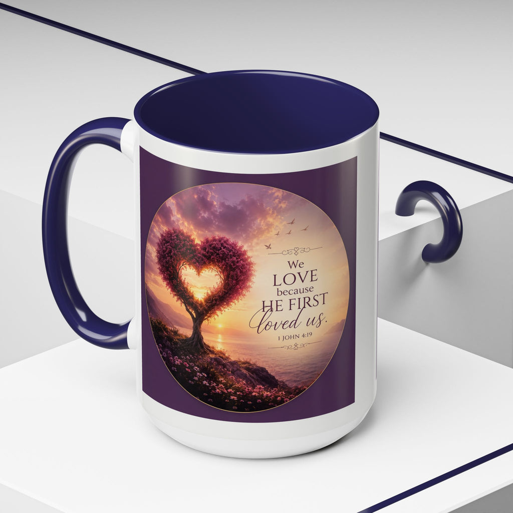 Inspirational Christian coffee mug featuring a glowing heart-shaped tree at sunset with the scripture “We Love Because He First Loved Us” from 1 John 4:19 and contrasting black handle and interior.