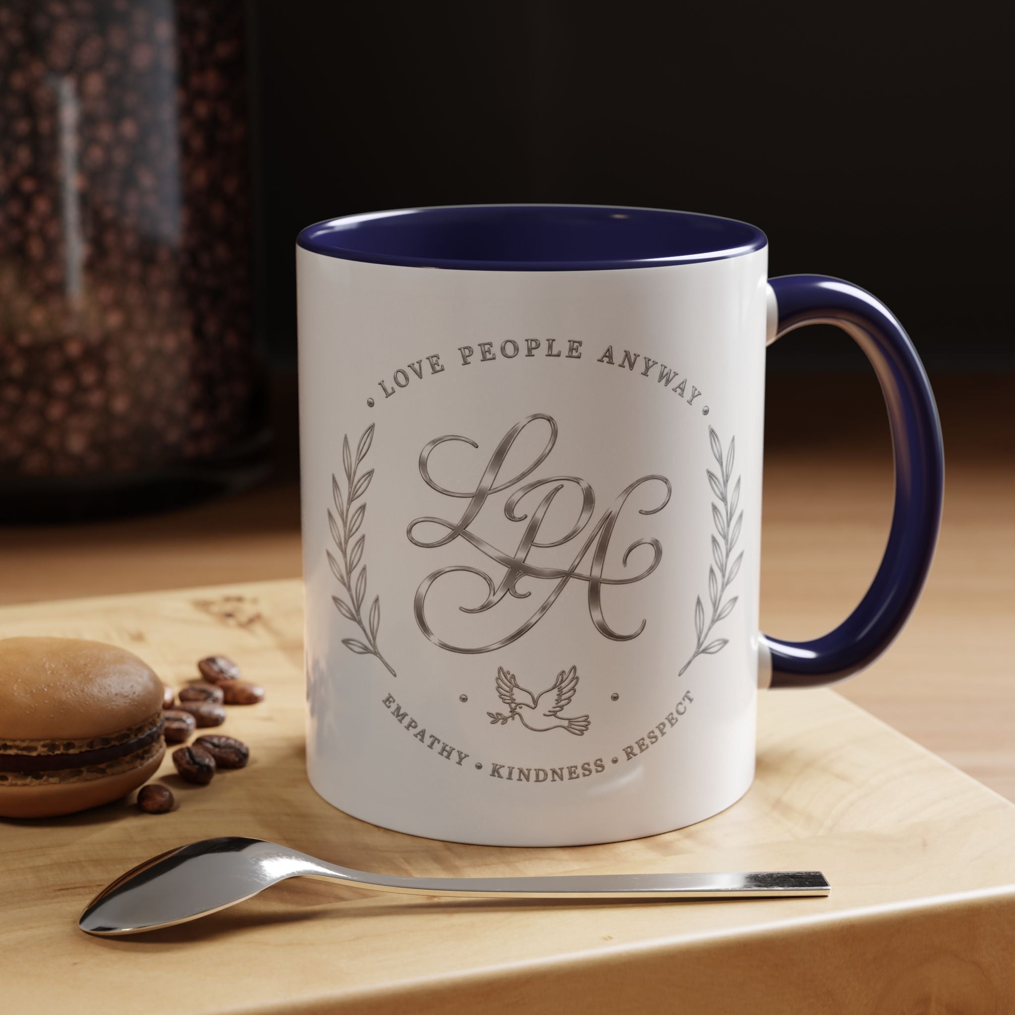 Inspirational ceramic coffee mug featuring silver “Love People Anyway” script, elegant monogram styling, decorative wreath accents, and contrasting handle and interior.