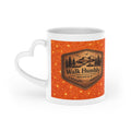 White ceramic heart-shaped handle mug featuring a rustic mountain "Walk Humbly" badge inspired by Micah 6:8 on a sparkling orange background.