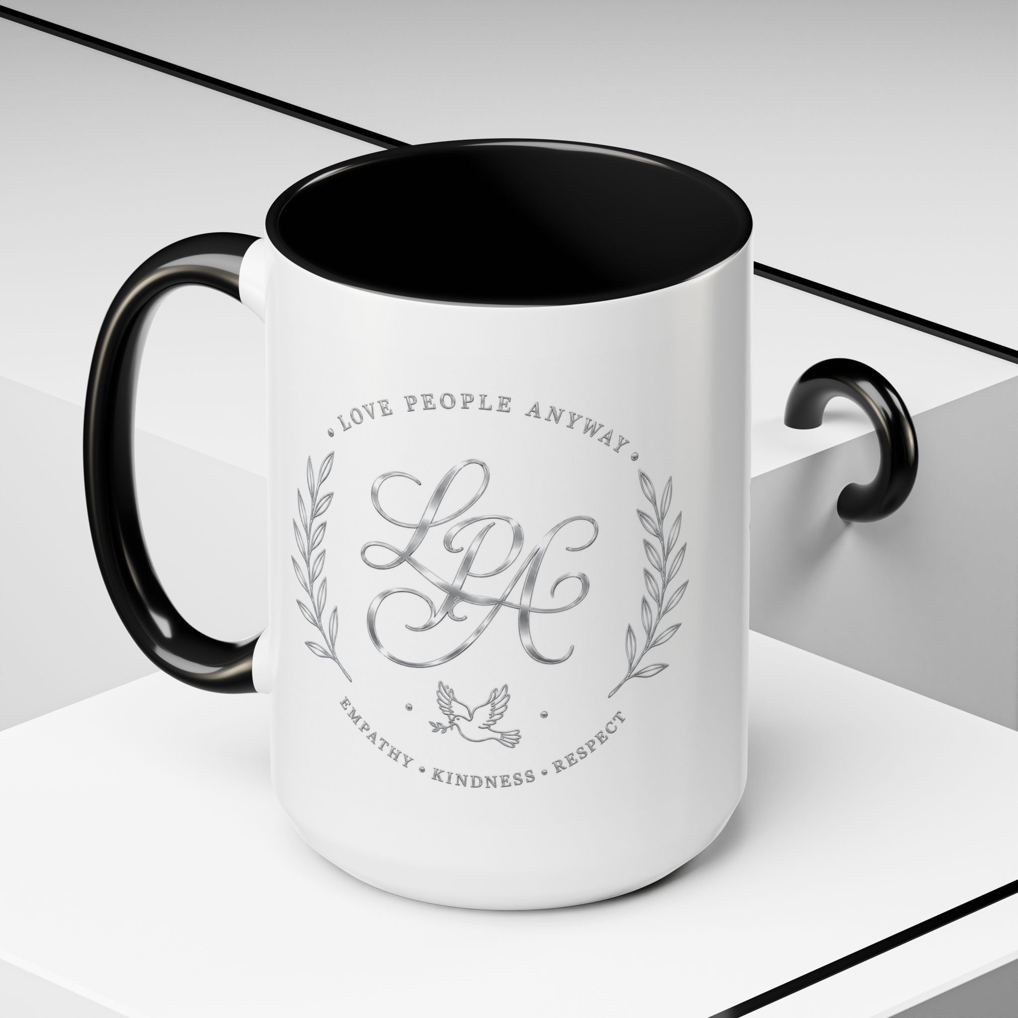 Inspirational ceramic coffee mug featuring silver “Love People Anyway” script, elegant monogram styling, decorative wreath accents, and contrasting handle and interior.