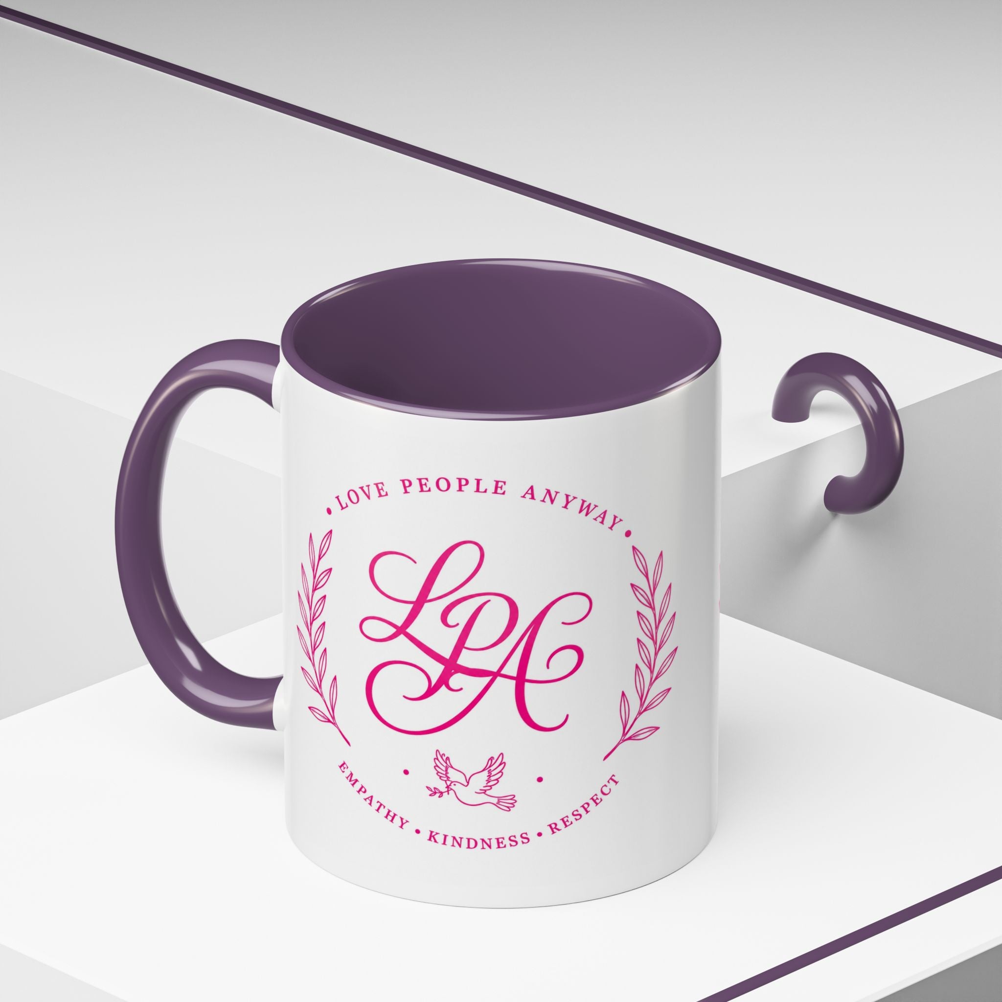 Inspirational ceramic coffee mug featuring soft pink “Love People Anyway” lettering, laurel accents, a dove motif, and contrasting purple handle and interior.