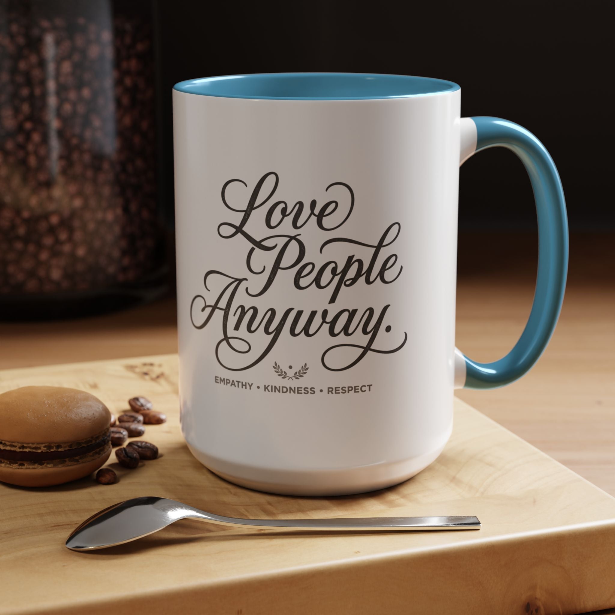 Inspirational ceramic accent coffee mug featuring hand-lettered “Love People Anyway” typography with empathy, kindness, and respect message on a glossy white mug with colorful handle and interior.