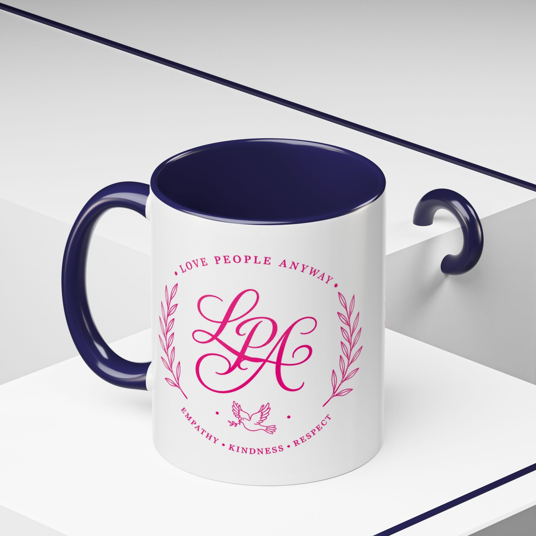 Inspirational ceramic coffee mug featuring soft pink “Love People Anyway” lettering, laurel accents, a dove motif, and contrasting black handle and interior.