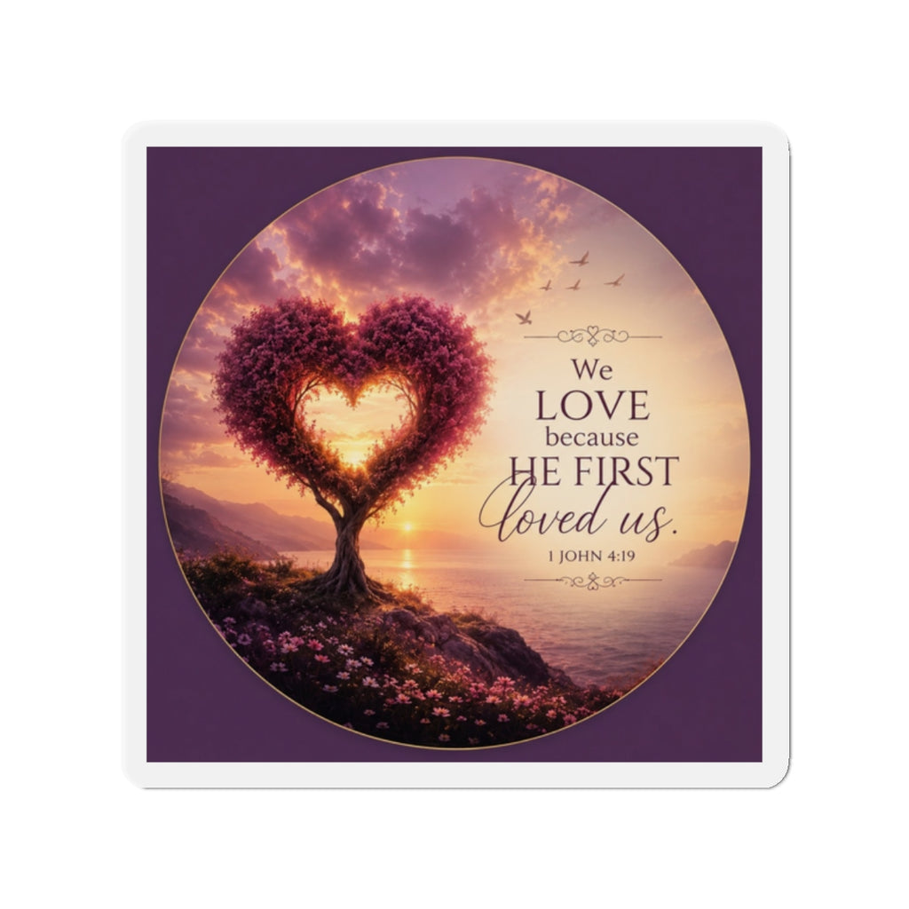 Die-cut Christian magnet featuring a heart-shaped tree at sunset with the scripture “We Love Because He First Loved Us” from 1 John 4:19 in purple, pink, and gold tones overlooking a peaceful shoreline.
